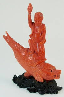 A Chinese red coral carving: An antique red coral carving depicting a deity seating on top of a large Koi fish, on a matching wooden stand carved as wavy sea SIZE: The coral itself 3.25" Overall including the stand 3.75"