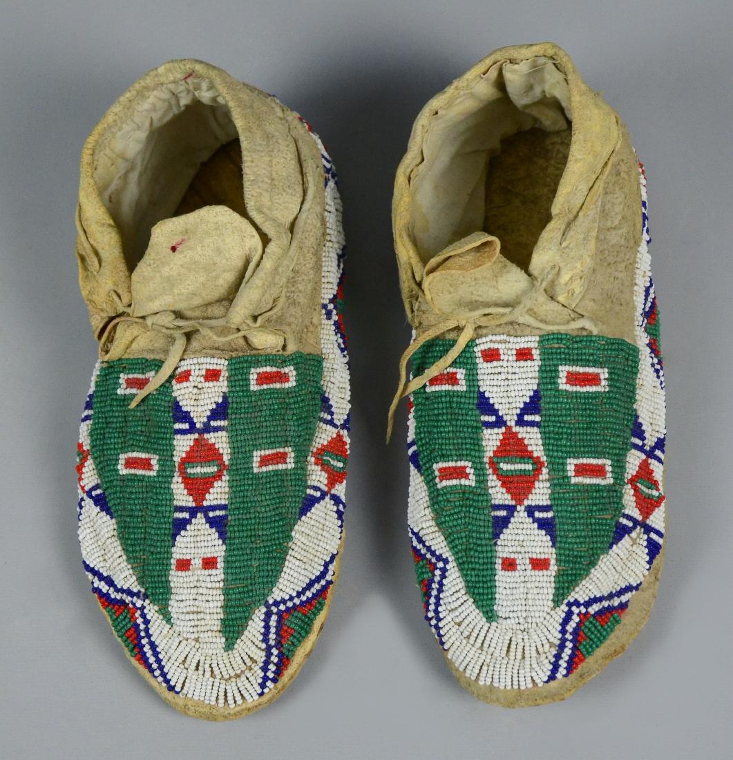 Sioux Native American Indian Beaded Moccasins: Sioux Native American Indian Beaded Moccasins, predominantly white detailed with geometric designs in red, white, green and cobalt beads, 10" L