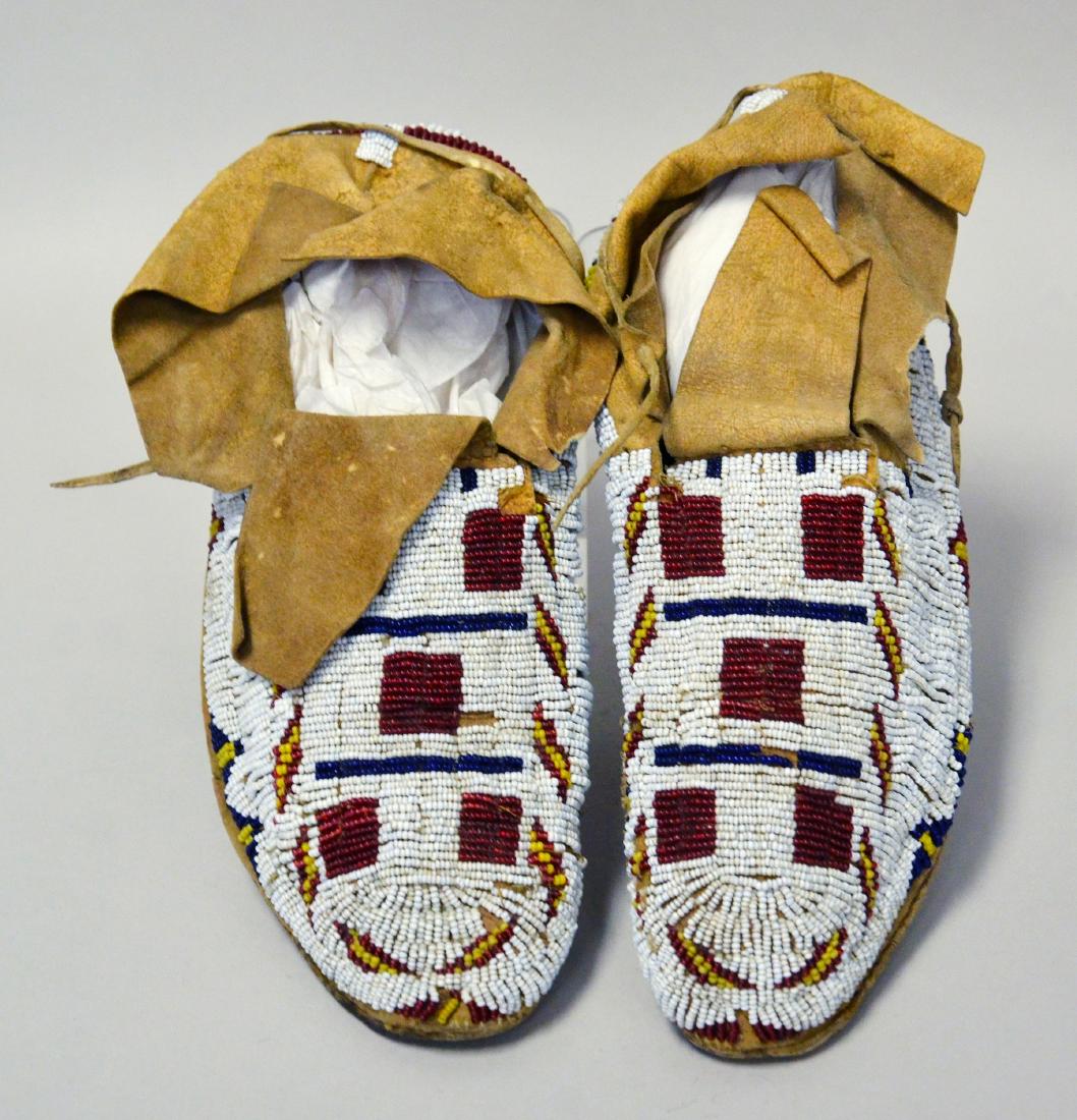 Sioux style Native American Indian Beaded Moccasins: Sioux style Native American Indian Beaded Moccasins, predominantly white detailed with geometric designs in red, yellow and cobalt beads, 9-1/2" L