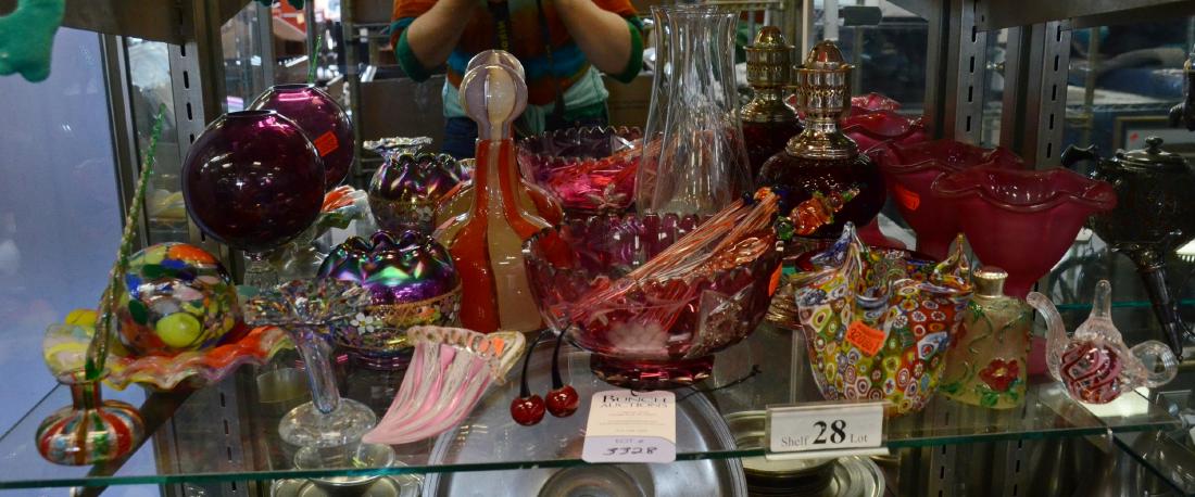 Shelf #28 - Colored Glass: Shelf #28 - Colored glass, including cranberry cut to clear bowl, Fenton hand painted plum carnival rose bowl signed by artist, vases,decanter, latticino shoe, oil lamp