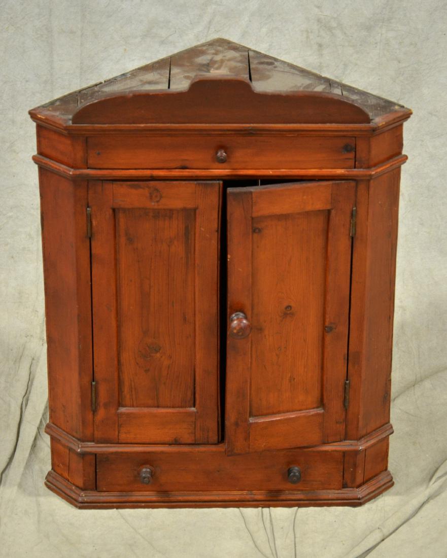 Pine hanging corner cabinet, American, 19th c: Pine hanging corner cabinet, American, 19th c, shaped crest board over molded top edge, with a single drawer over double flat paneled doors over another single drawer, turned wood pulls, Height 24", w