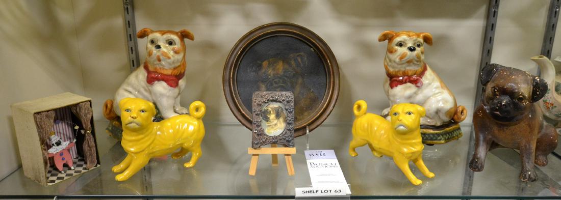 Shelf #63 - Dog Figures and Oil Painting: Shelf #63 - Pair Porcelain Dog Bookends (6-3/4" l x 4" w x 8-1/4" h), Porcelain Dog Bank, Pair Yellow Dog Figures, Pug Dressed as a Clown Diorama, Pug Portrait in Metal Floral Frame, Pug Portrait, Oil