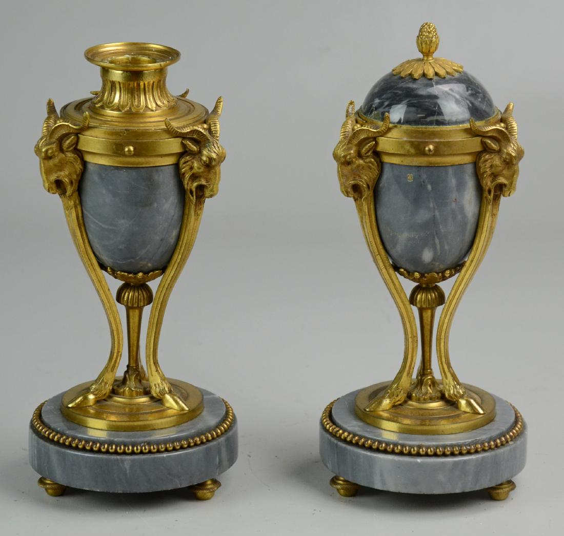 Pr Marble Convertible Urns: Pair of gray marble urns, ormolu gilt bronze mounts, 3 goat head legs ending with cloven hoof, stepped circular plinth base on toupie feet, pinecone finial, lid reverses to candleholder, 9-1/2" h, one