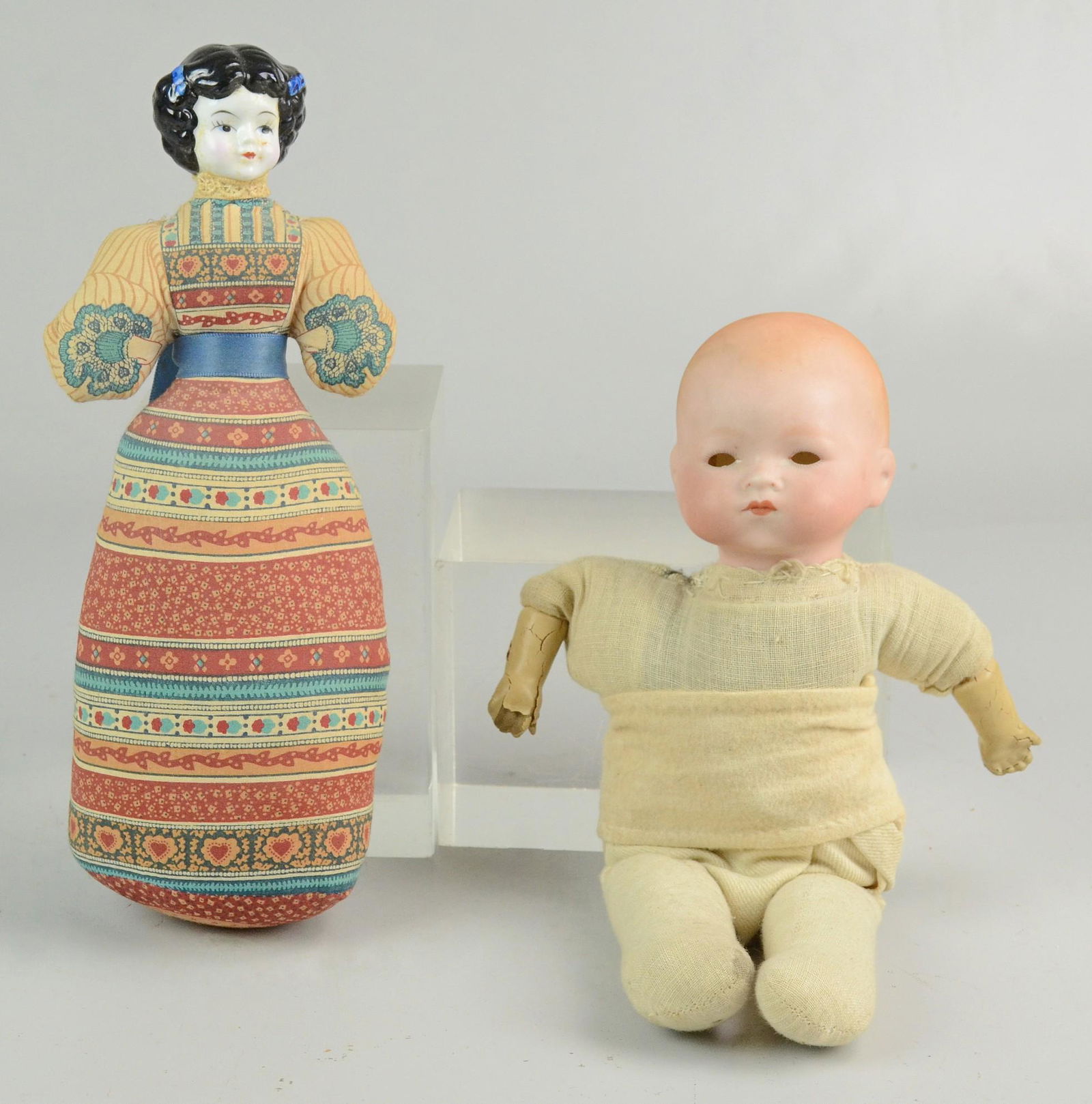 (2) Porcelain Head Dolls: (2) Porcelain head dolls, c/o Armand Marseilles baby doll marked "AM Germany", closed mouth, cloth body, composite hands in poor condition, eyes need to be reset, 10-1/2" h, Avon American Heirloom rep