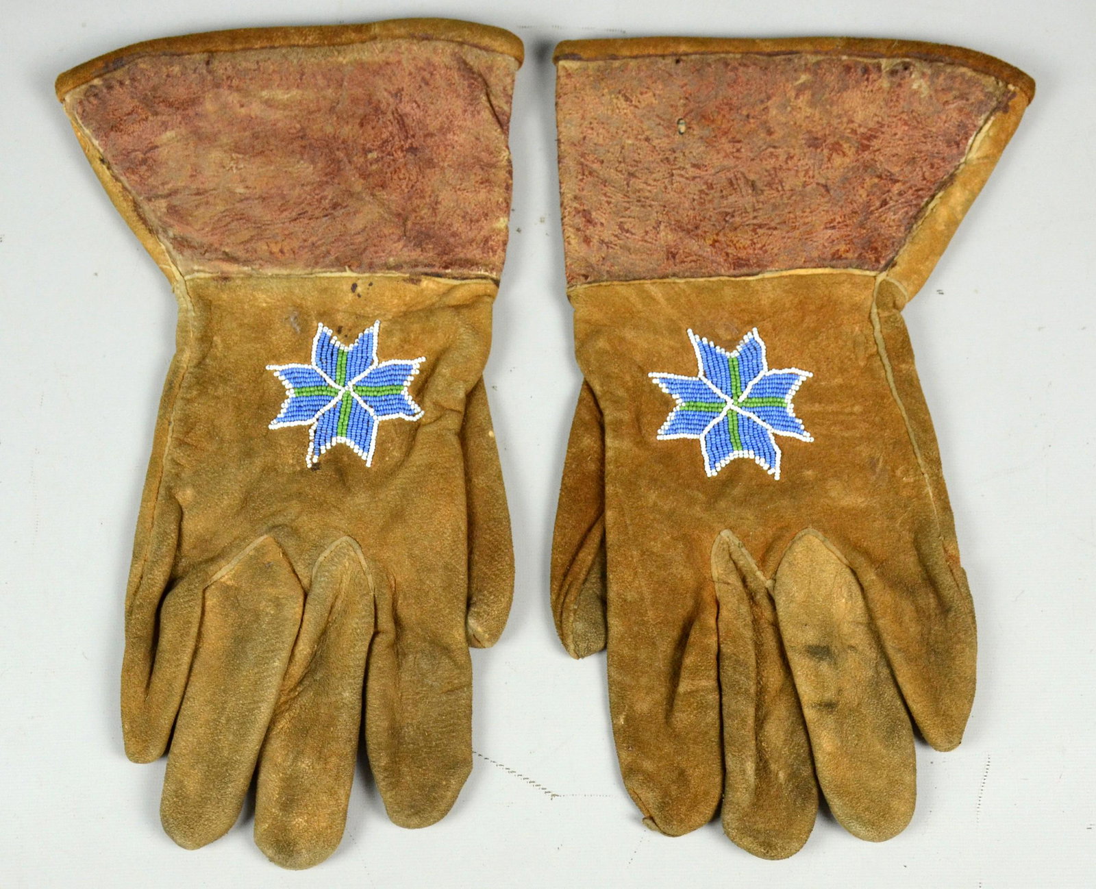 Native American hide & beaded gauntlet gloves: Native American hide & beaded gauntlet gloves, Northern Plains, decorated with geometric design in blue, green & white beadwork, on tanned hide, floral patterned fabric interior, 12" L