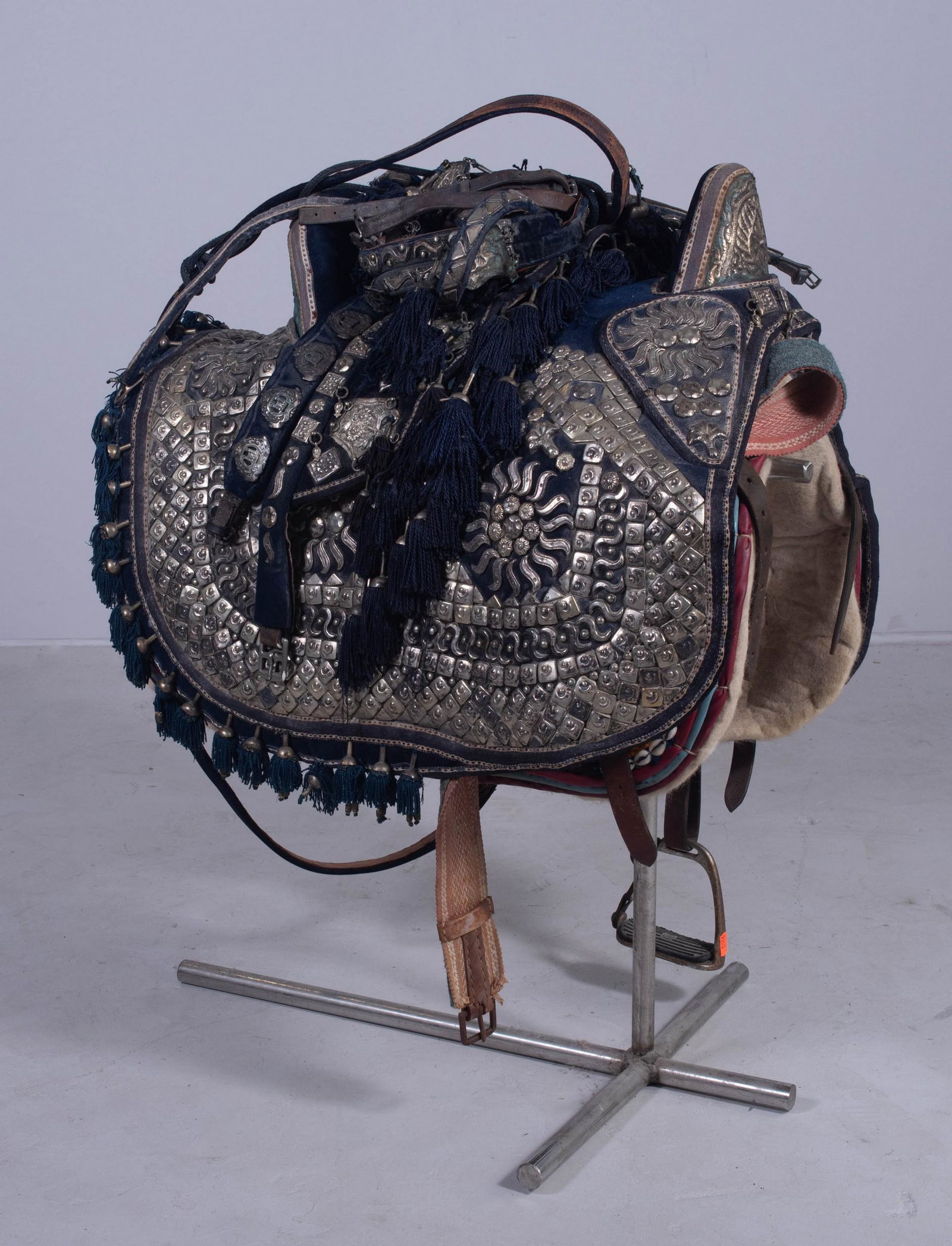 Arabian Ceremonial Saddle: Arabian ceremonial saddle lined with felted wool pad on stand. Fully adorned in hand hammered metal decoration, metal wrapped fringe surround and hammered beads. Complete with leather supports dotted 