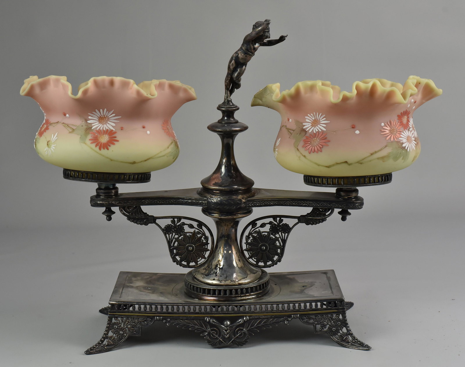 Pairpoint Art Glass and Silverplate Stand: Pairpoint art glass and silverplate stand. (2) ruffle edge art glass bowls in ornate silverplate stand with putti at center. Floral scrolls and reticulated feet. Glass with large chip, pieces included