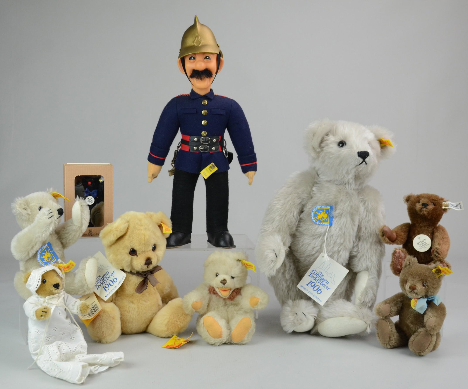 Steiff Grouping: Steiff grouping c/o Giengen replica teddy bear 1906, small Giengen replica teddy bear 1906, Steiff soldier, (2) small seated bear, small bear in christening gown, 7cm Steiff Club gift bear in black an