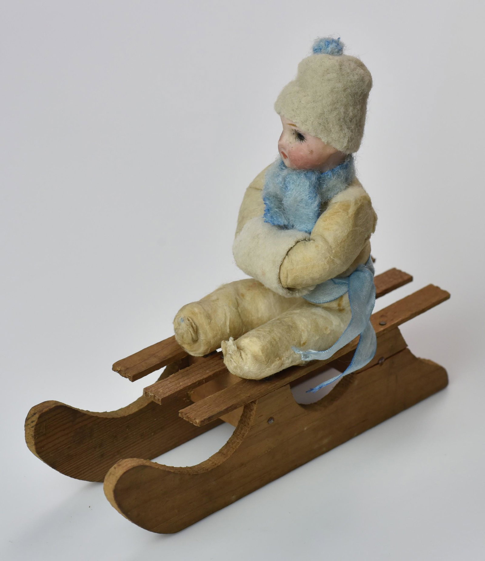 Heubach Child on Wood Sled: Heubach child, white cotton suit, blue scarf on wood sled- 6" l (c.1910, Germany)