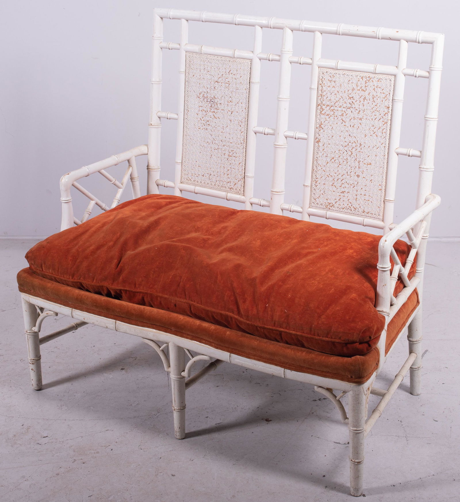 Faux bamboo painted 2 seat bench: Faux bamboo painted 2 seat bench, white painted, caned back, orange upholstered cushion, 40" h x 41" w x 25" d, wear to paint, damage to caning