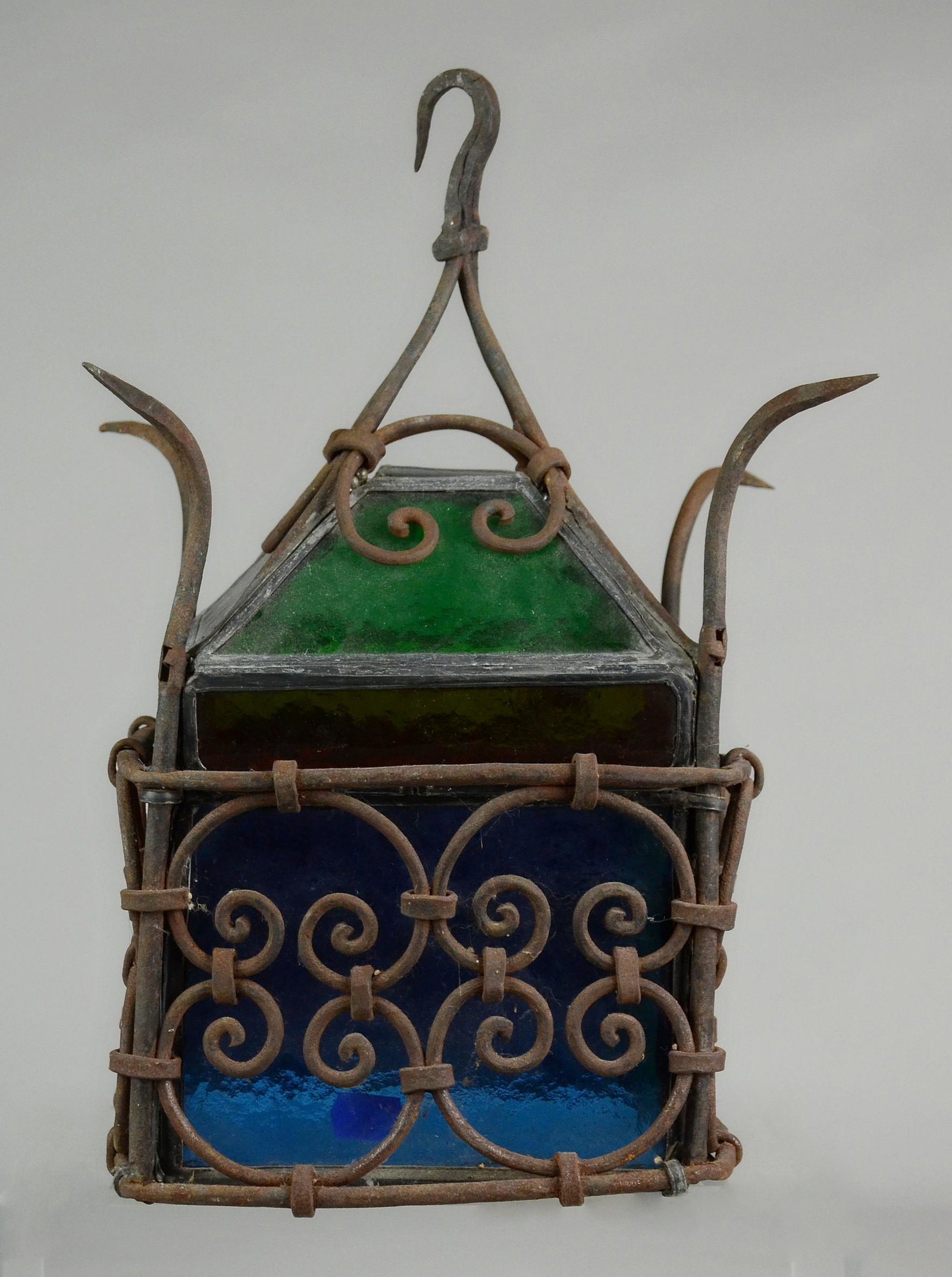 Stained Glass Gothic Wrought Iron Lantern: Victorian gothic wrought iron lantern with multicolor glass panel interior. Encased in scrolling hand wrought iron case with outturned spiked corners, gathered final and hook for hanging. 8"x8"x16"