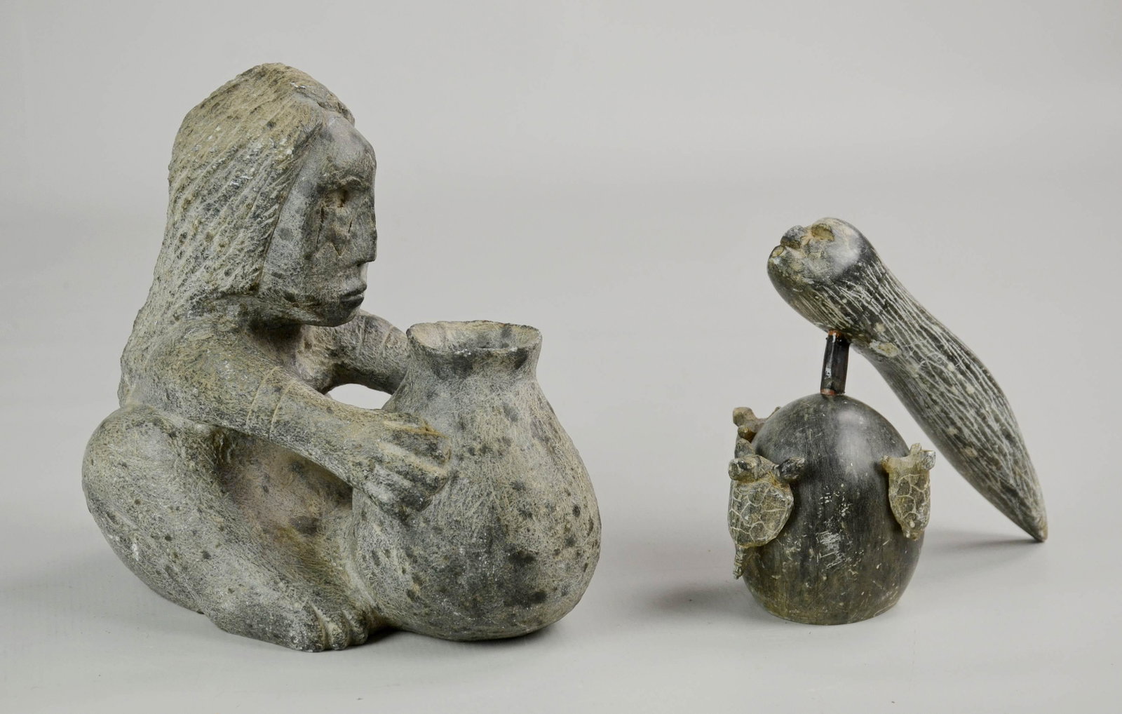 (2) Alaskan Stone Carvings: (2) Alaskan stone carvings c/o seated figure at vessel, 8"x4-1/2"x8-1/2" and similar hand designed carving of long haired head perched on oval stone with carved turtle surround, signed underside ' How