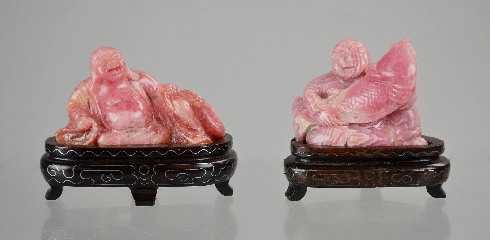(2) Chinese Pink Stone Buddha Figures: (2) Chinese carved pink stone Buddha figurines, c/o one with fish, one with sack, on wood stands, largest 3" h x 3-1/2" w