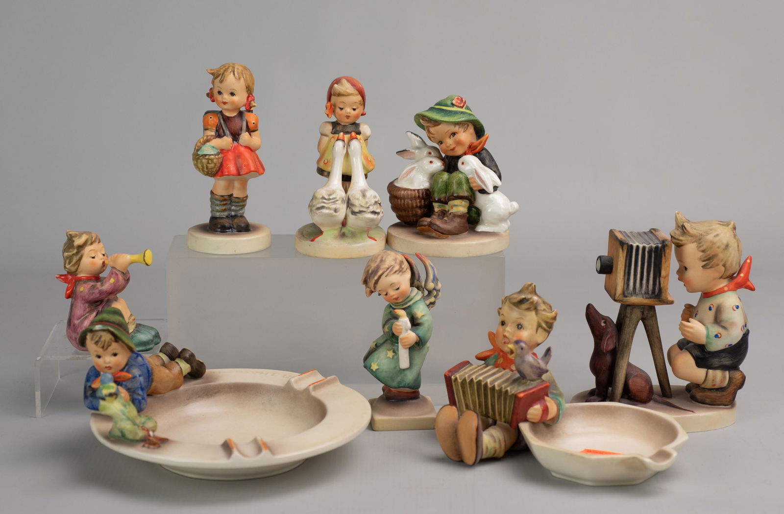 (8) Goebel Hummel Figures: (8) Goebel Hummel porcelain figurines c/o (2) ashtrays #166 and #114 TMK 3, boy photographer with dog, #25 TMK4, girl with ducks # 47 3/0 TMK 3, boy with rabbits # 58/0 TMK 3, winged boy with candle,