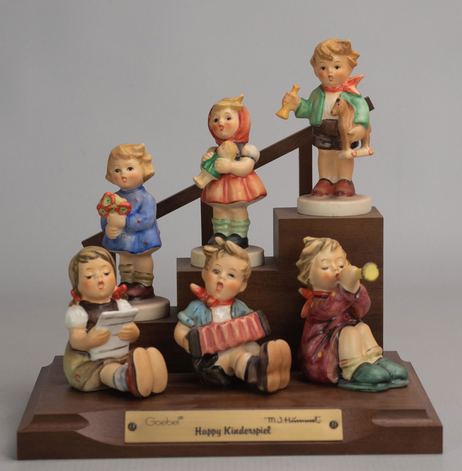 (6) Hummel Figures " happy Kinderspiel": (6) Goebel Hummel porcelain figurines on wooden staircase display, " happy Kinderspiel", Girl with Nosegay 239A (TMK6), Girl with Doll 239B (TMK5), Boy with Horse 239C (TMK5), Girl with Sheet Music 38