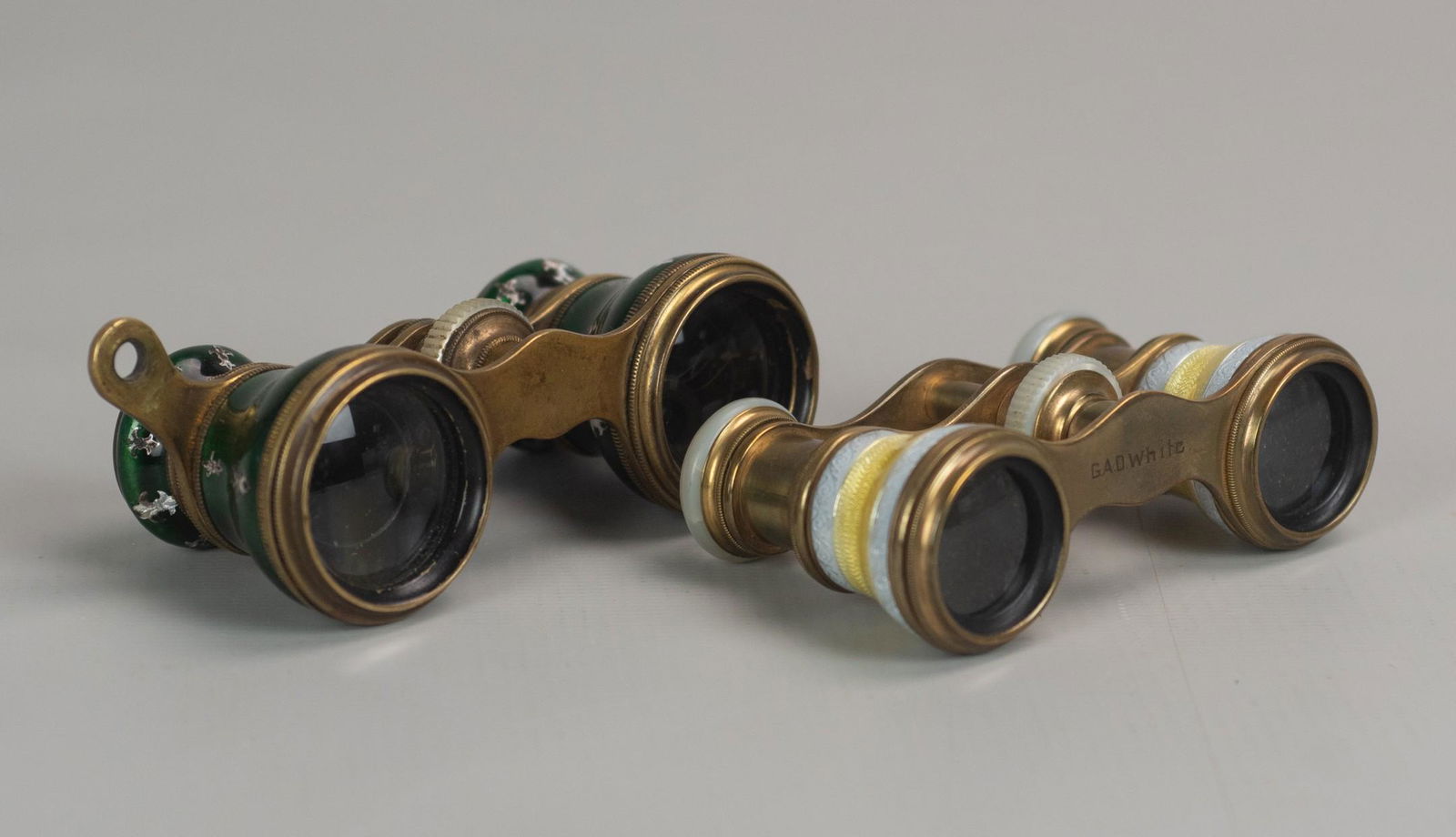(2) French Guilloche Opera Glasses: (2) French guilloche opera glasses c/o La Monte Paris viewers in emerald and fleur de lis decoration with gold tone mounts, 4", and similarly designed yellow and pearl tone glasses with M.O.P and gold