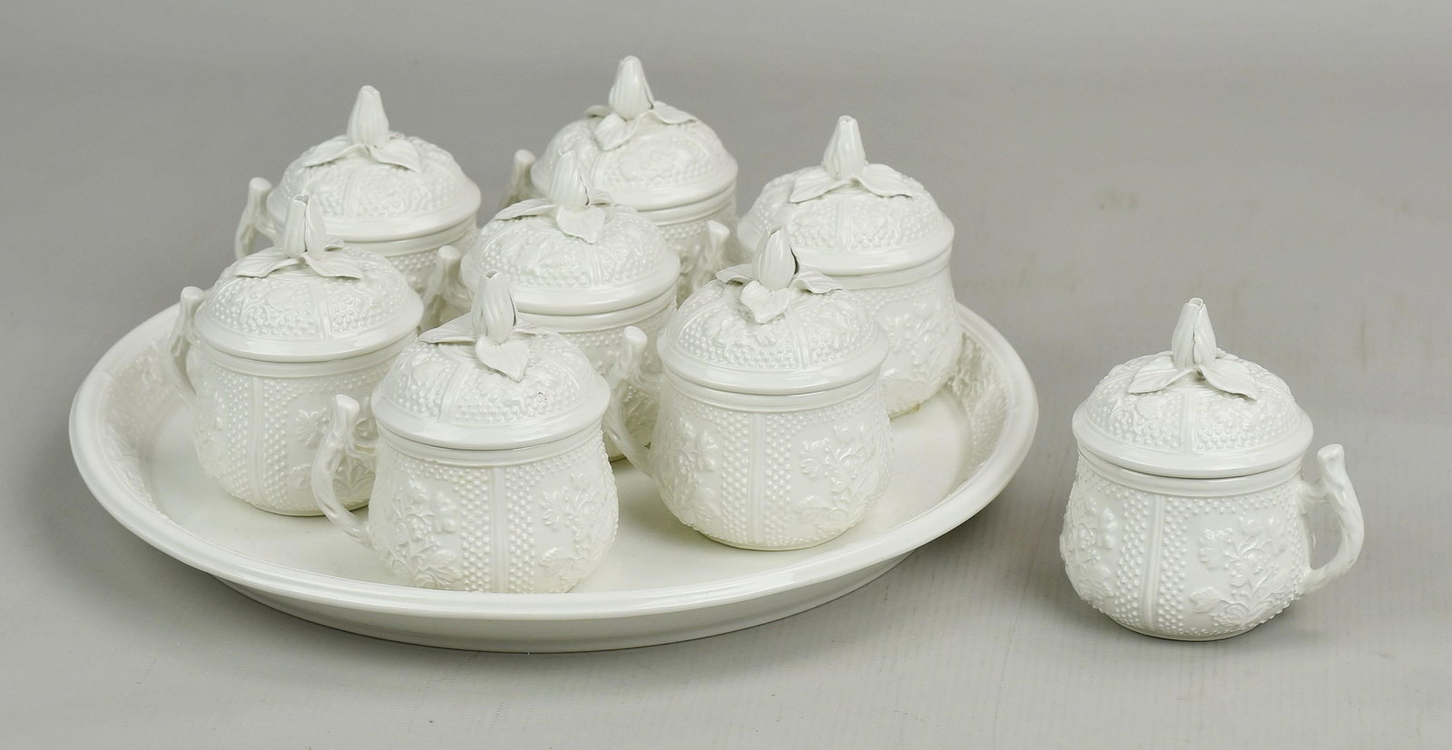(9) Pcs Mottahedeh Bisque Pot de Creme and Tray: (8) Mottahedeh bisque pot de creme and tray c/o (8) covered pots with embossed floral and dot design, handle, and floral finial and 11" matching tray with raised embossed lip. Some pots with small chi