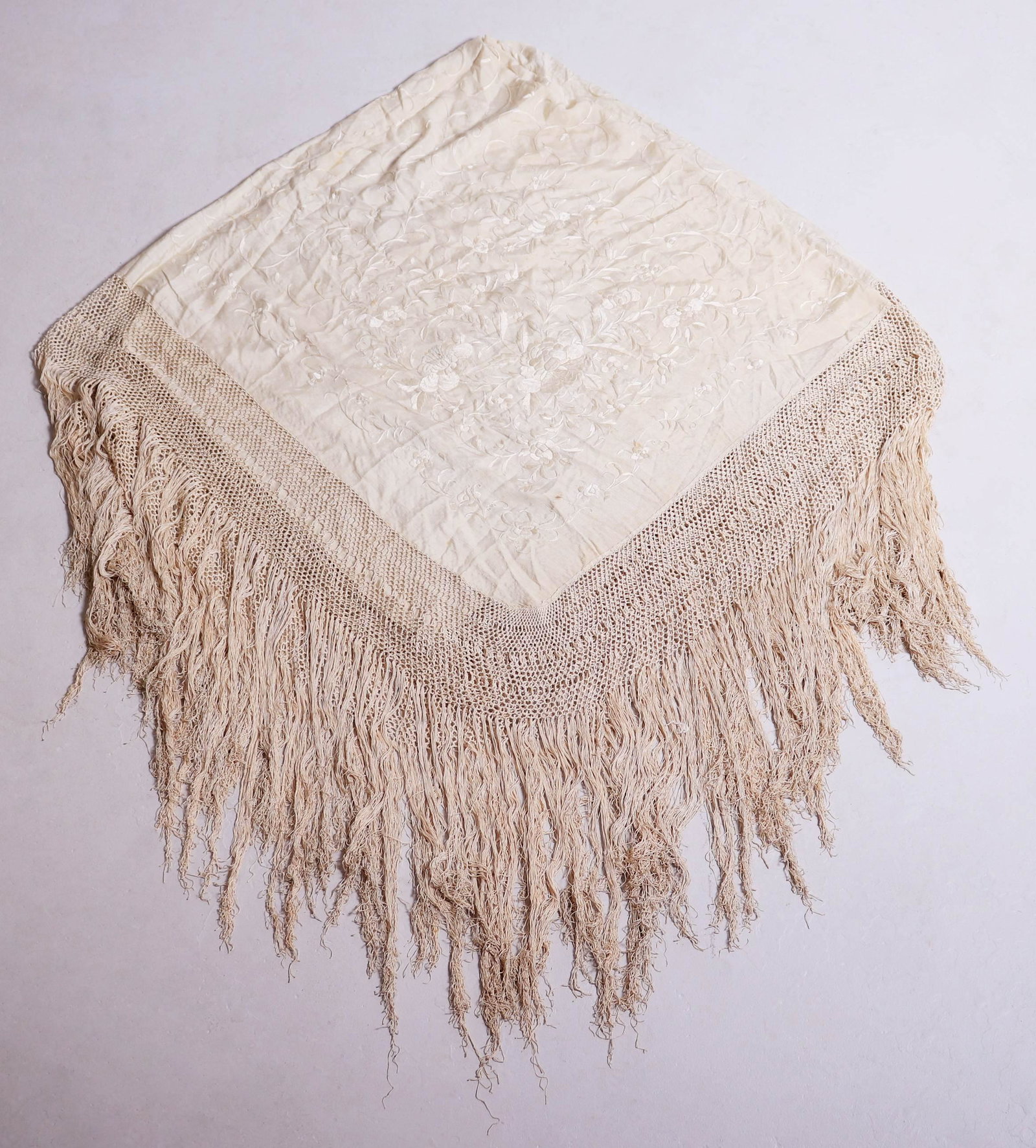Oversized Embroidered Cream Silk Piano Shawl: Oversized embroidered cream silk piano shawl with 51/2" hand knotted trim followed by an extra 14" silk fringe surround. Center is embroidered in all over crawling floral decoration, spot staining thr