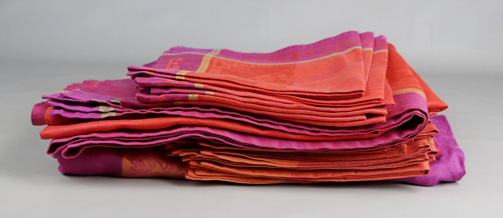 (2) Le Jacquard Francais Tablecloths and Napkins: (2) Le Jacquard Francais tablecloths and napkins c/o (2) magenta and mandarin coated jacquard tablecloth, 70"x70" with (16) dinner napkins and (1) magenta and hot coral coated jacquard tablecloth, 100