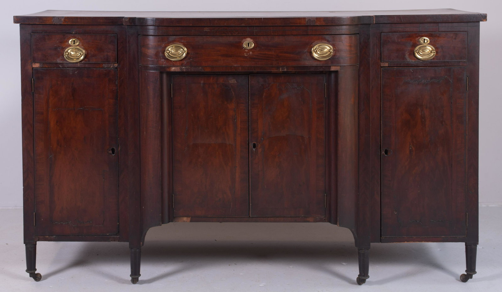 Mahogany Sheraton Sideboard: American Mahogany Sheraton Deep Body Sideboard, bowed central door over 2 flat banded doors, flanked by straight drawers over flat banded doors, some veneer chips and shrinkage cracks in top, Philadel