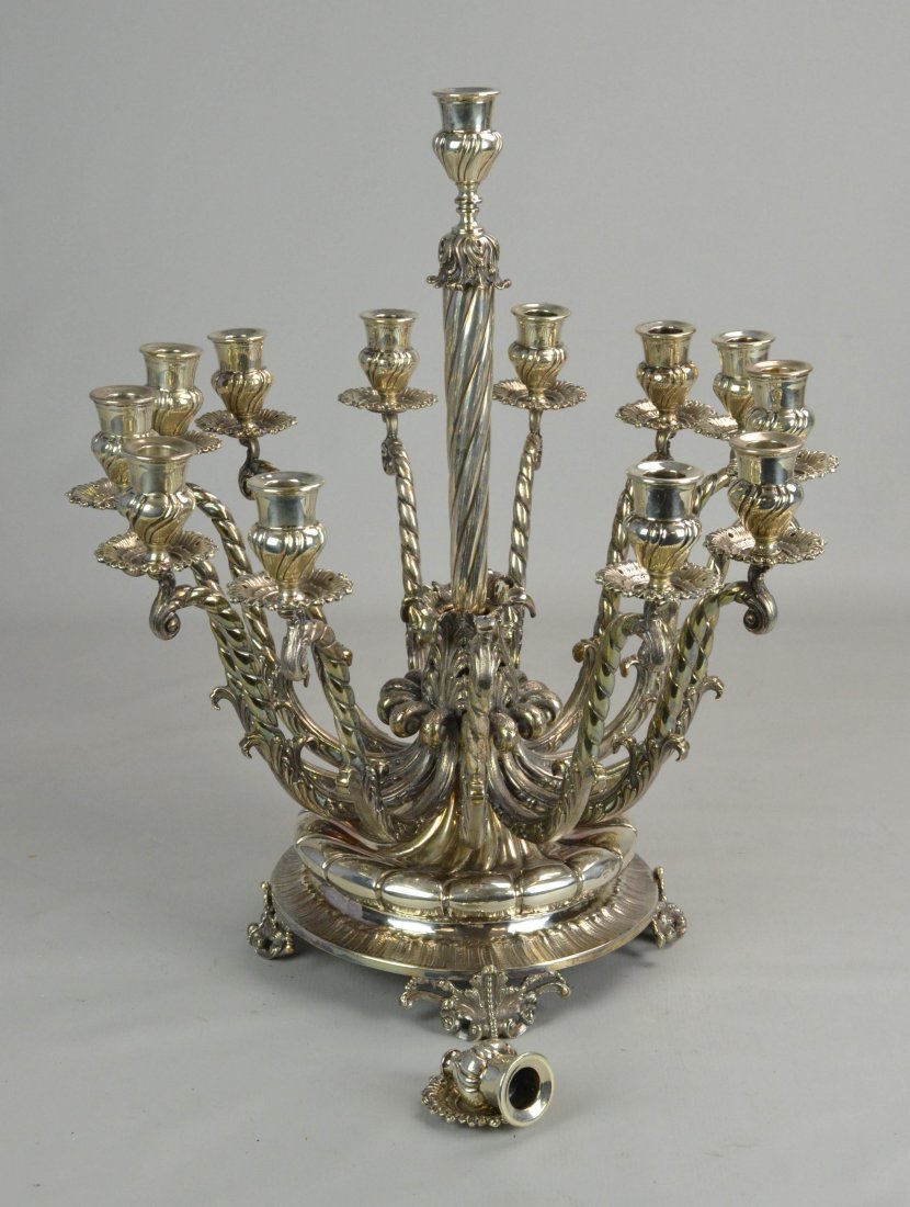 14-Arm Aesthetic Silver Plate Candelabra: 14-Arm aesthetic silver plate candelabra on raised footed base with (13) scroll decorated arms with foliate motif bobeche and gadrooned cup. Single center light on raised spiral stem. (1) Cup needs re