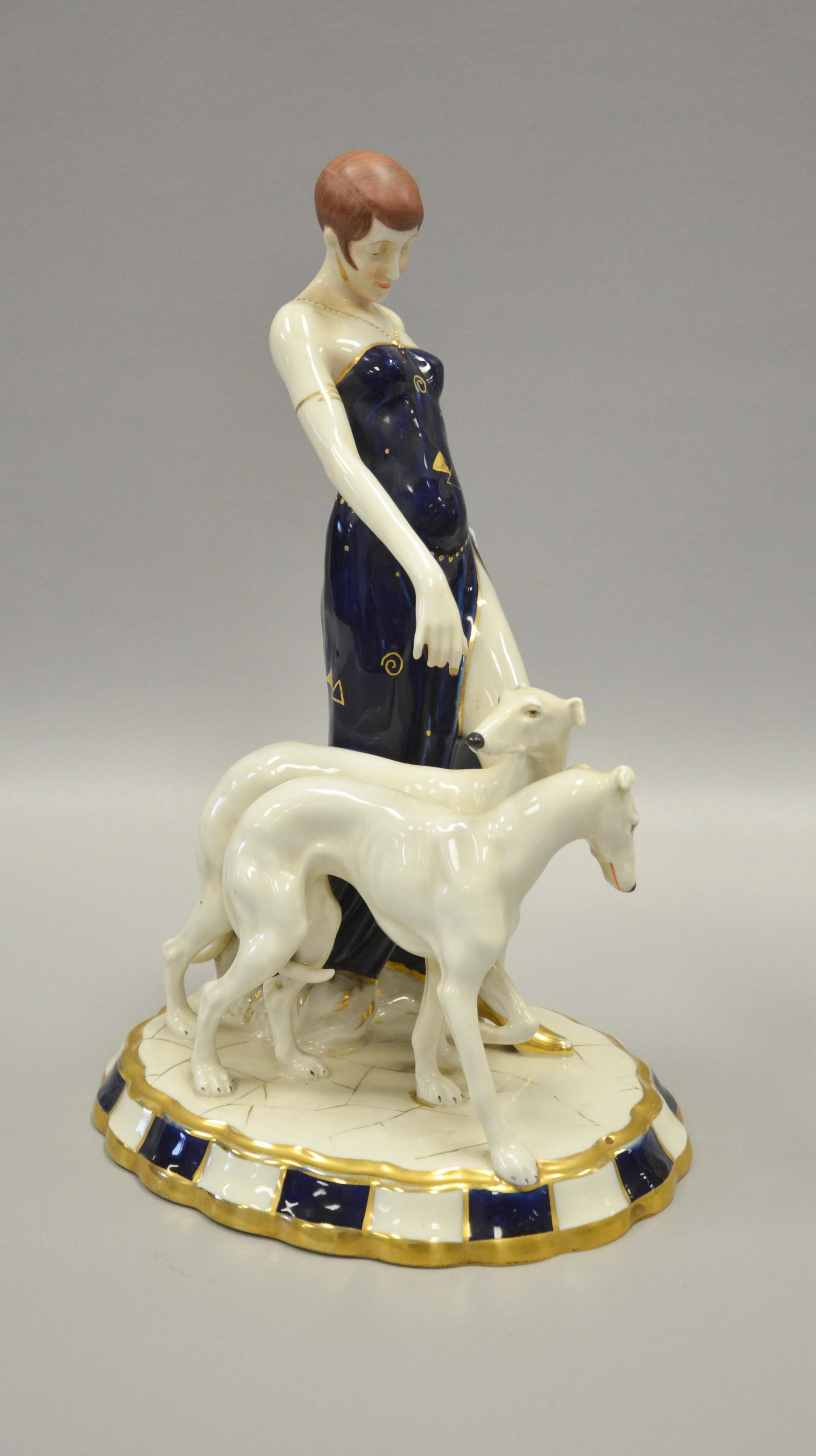 Royal Dux Flapper with Borzoi Dogs Figure: Royal Dux Bohemia porcelain figurine, "Flapper with Borzoi Dogs", 15" h, piece of wood added to underside of base, Wear to gilt. Wood brace underneath.