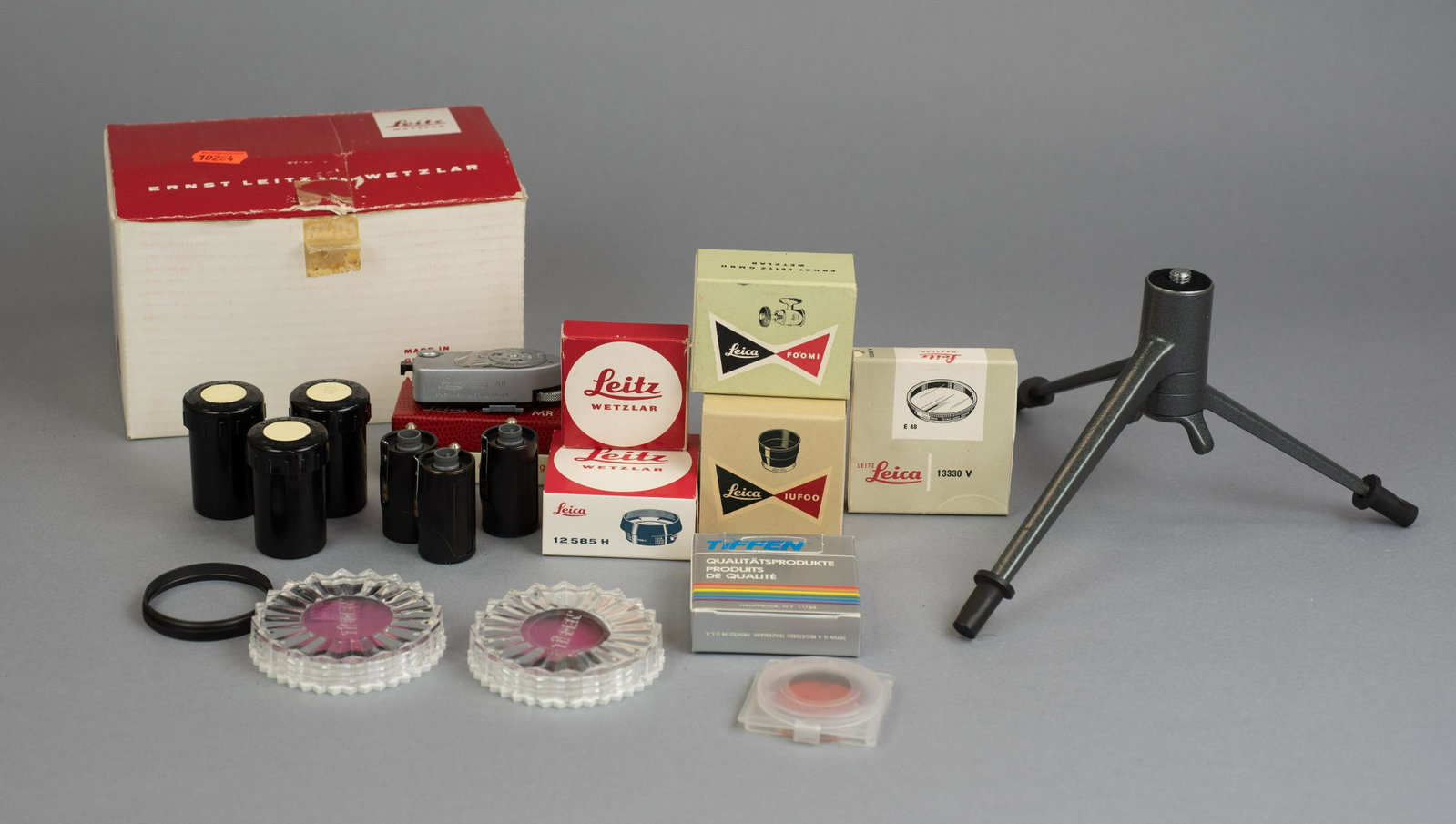 Leica Accessory Grouping: Various Leica/Leitz branded accessories including table top tripod with FOOMI head, IUFOO lens hood, Leica-Meter MR (missing battery door) with manual, Leitz Orange filter, assorted TIffen filters and
