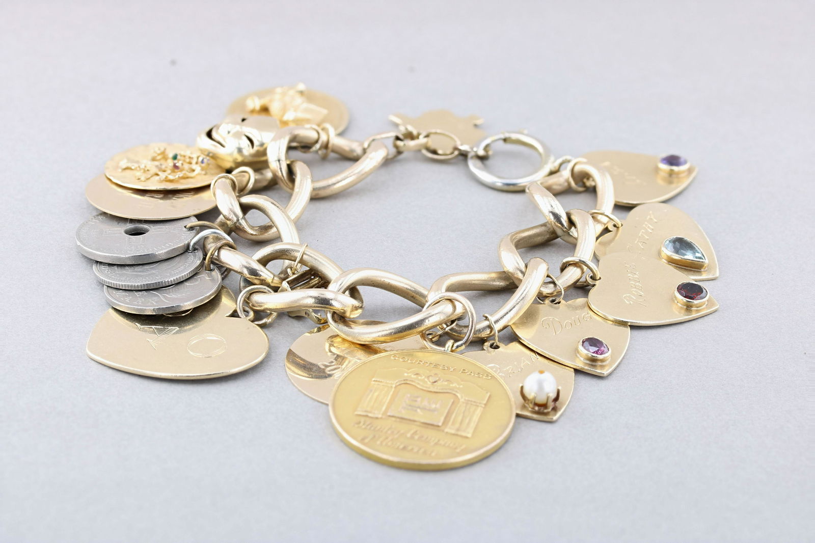 Charm Bracelet 14K and Gold Filled: (1) Gold filled oval curb link bracelet wide links, with Thirteen 14K Gold charms, most signed /testing at 14K, bezel set with pink sapphire, amethyst, and aquamarine and three silvertone travel coins