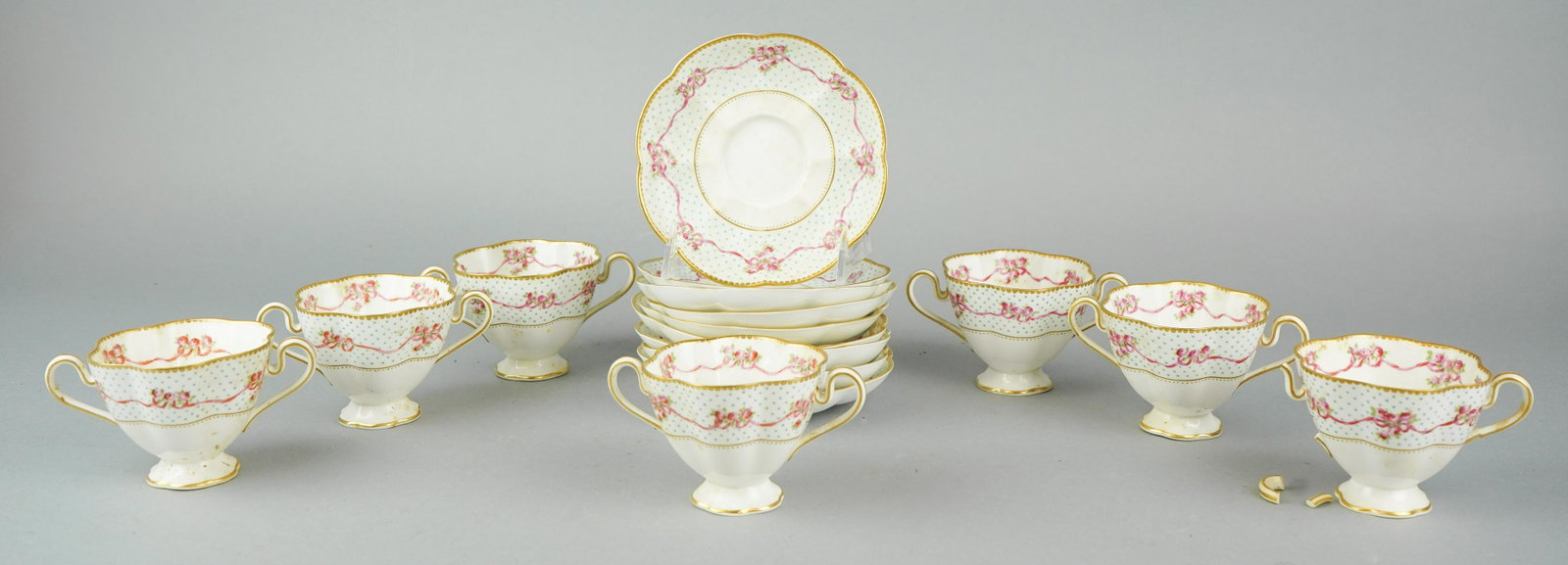 George Jones Crescent Footed Cream Soup Bowls: (17) Pcs George Jones Crescent & Sons porcelain, c/o (7) footed cream soup bowls (one handle needs repair) & (10) saucers, pink roses with ribbon swags & blue dots, scalloped edge, light wear to paint