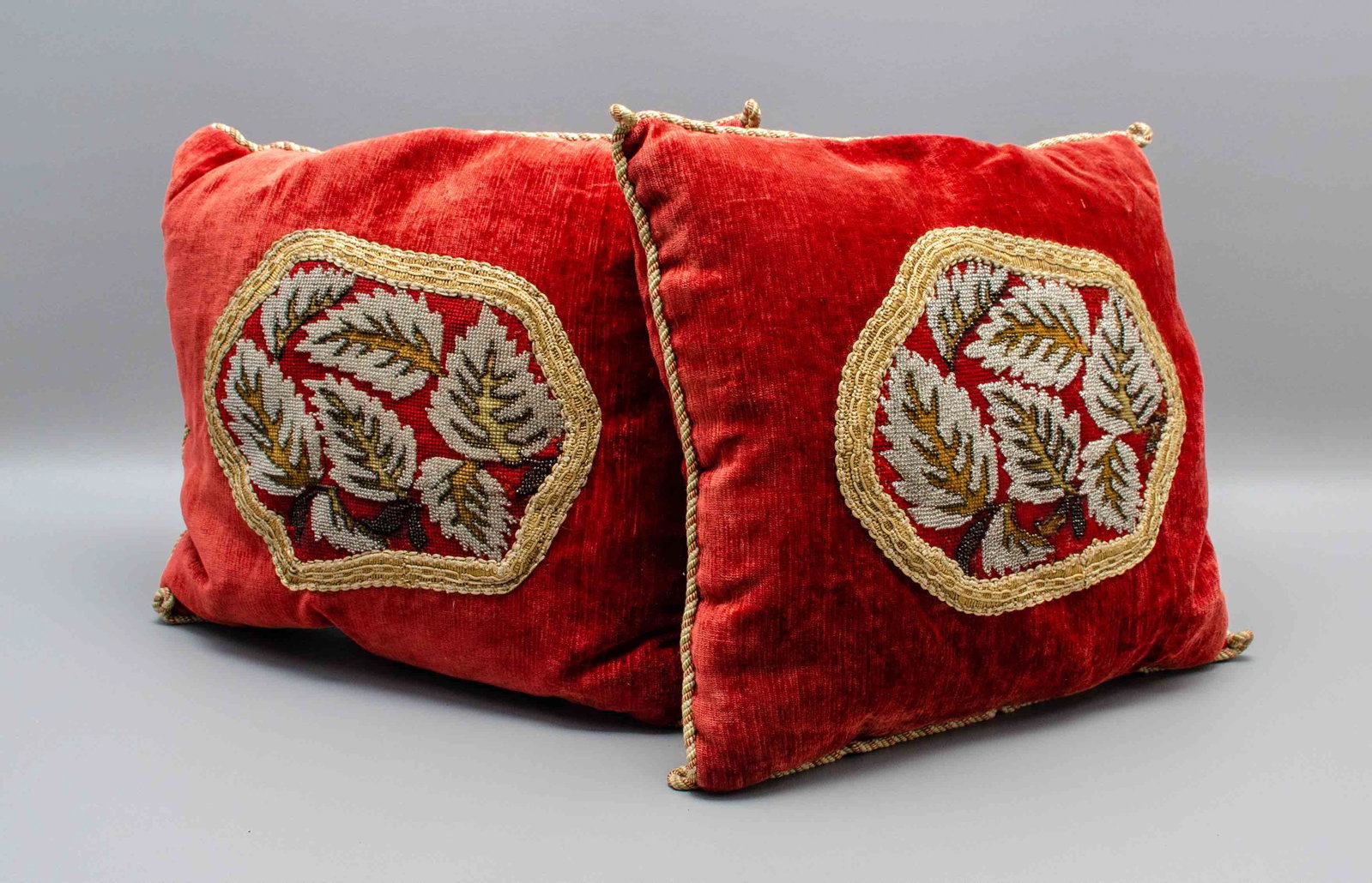 (2) Glass Beaded Needlepoint Throw Pillows: (2) Glass beaded needlepoint throw pillows, c/o 19th c. panel at top depicting needlepoint and glass beaded leaf pattern framed in silk knot trim in a field of red velvet with silk twist surround, 15"