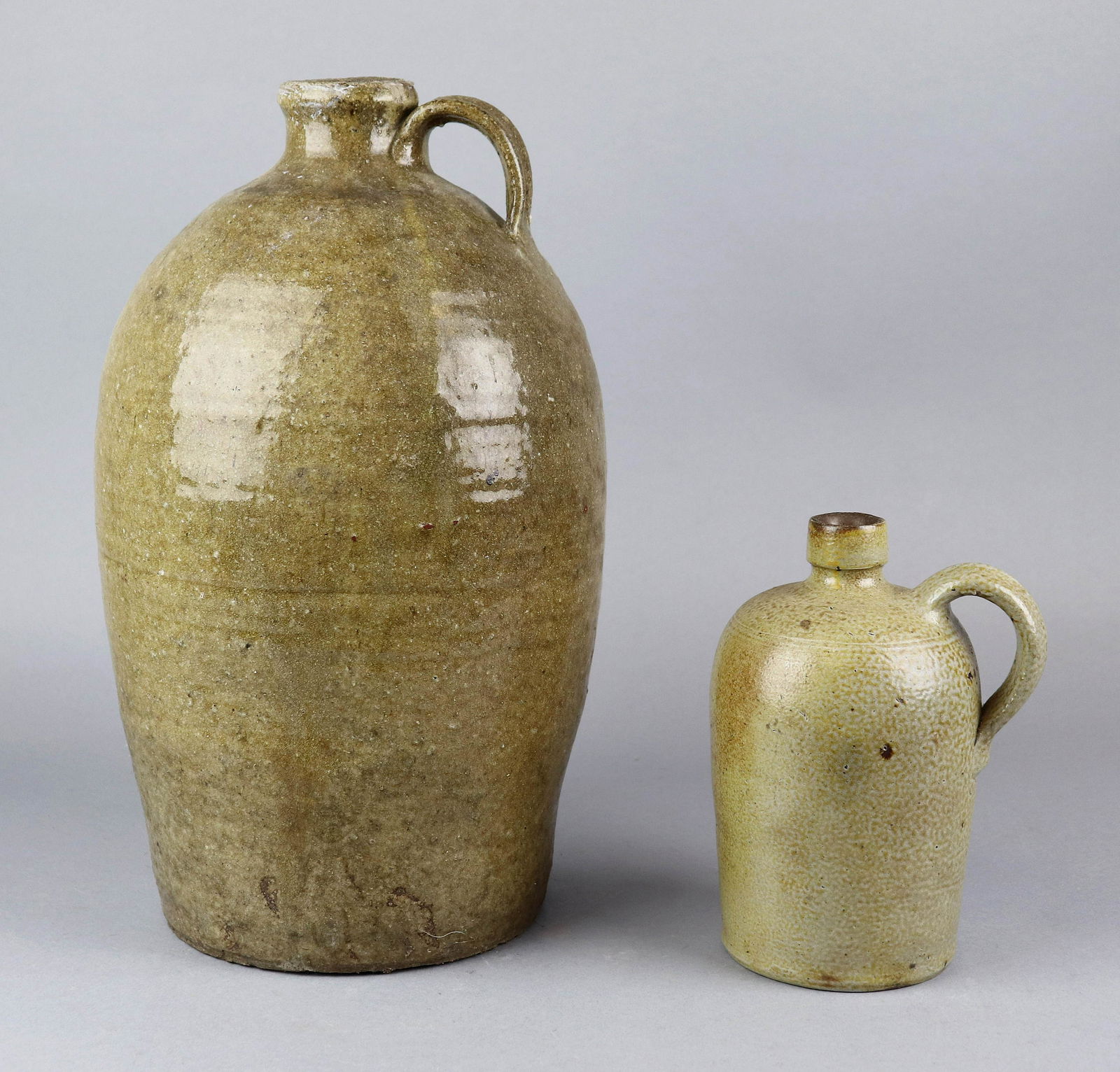 (2) Stoneware Jugs: (2) Stoneware jugs to include alkaline glazed handled jug, unmarked, small handle applied at neck, 15-1/2" H and salt glazed stoneware pottery jug, Robert C. Remmey, impressed RCR Phila, half gallon,