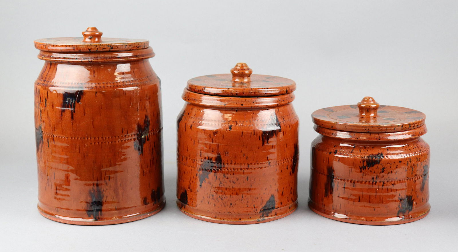 (3) Brown Glazed Redware Canisters: (3) Brown glazed redware canisters, graduated in size, with brown patch and impressed decoration, Williamsburg Pottery, some chips at lid, hairline at smallest lid, 6" H through 10-1/2" H