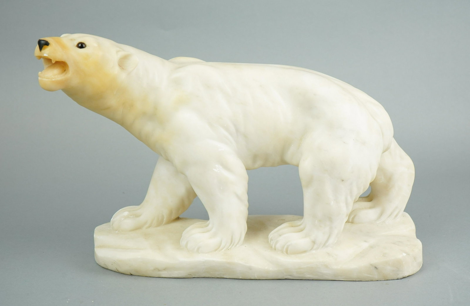Marble Carved Polar Bear Sculpture: Marble carved polar bear sculpture, single piece on carved slab with inset glass eyes and open mouth baring teeth, 15-1/4" L x 11" H, some yellowing to face, scuffs and chipping to teeth.