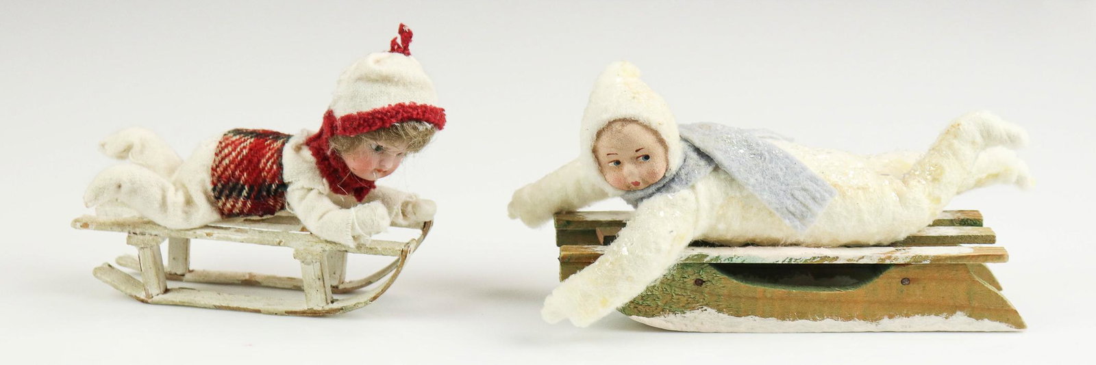 (2) Snowbabies on Sled Ornaments: (2) Snowbabies on sled ornaments to include Kramer and Reinhardt 1940's bisque head girl on sled ornament, 4-1/2" L and snowbaby child in white cotton suit on wood sled, 6-1/2" L