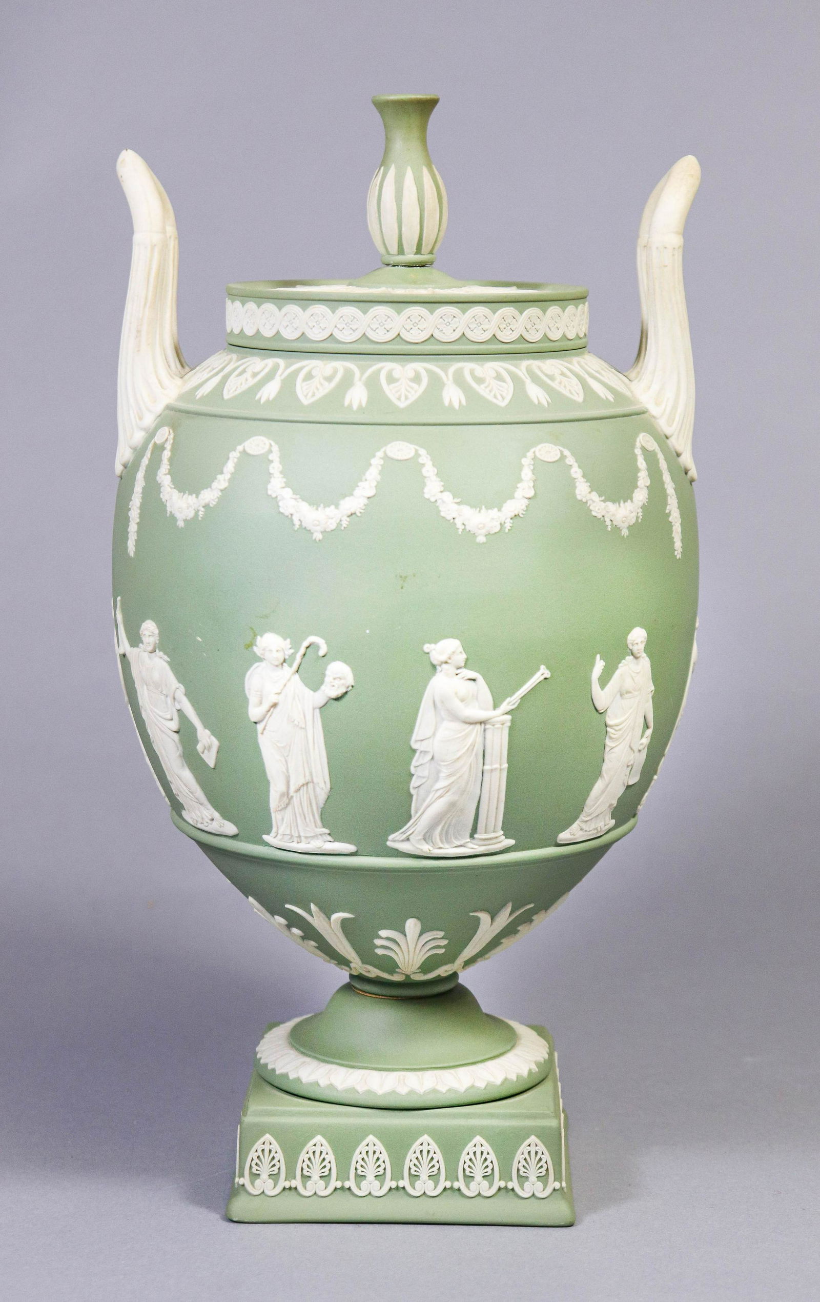 Wedgwood Jasperware Double Handle Urn: Wedgwood Jasperware double handle urn, on raised leaf decorated foot with stylized floral surround, lady decorated middle and floral garland and leaf shoulder, elongated double handles at sides, lid w