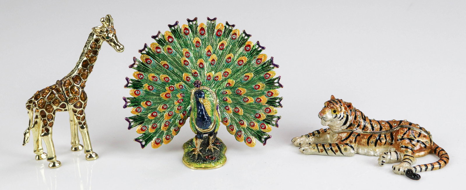 (3) Jere Enamel Trinket Boxes: (3) Jere enamel trinket boxes to include gem and enamel decorated spread plume peacock, gem studded giraffe and multi gem and stripe decorated tiger. All boxes open to reveal matched necklaces with mi