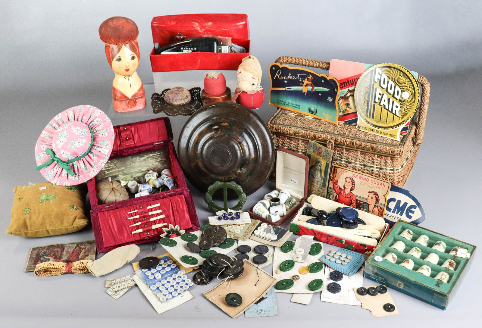 Sewing Accessories and Basket: Sewing accessories and basket to include wicker sewing basket, assorted pin cushions including figural and pillow form, assorted buttons, advertising needle packets, thimbles and velvet lift lid trave