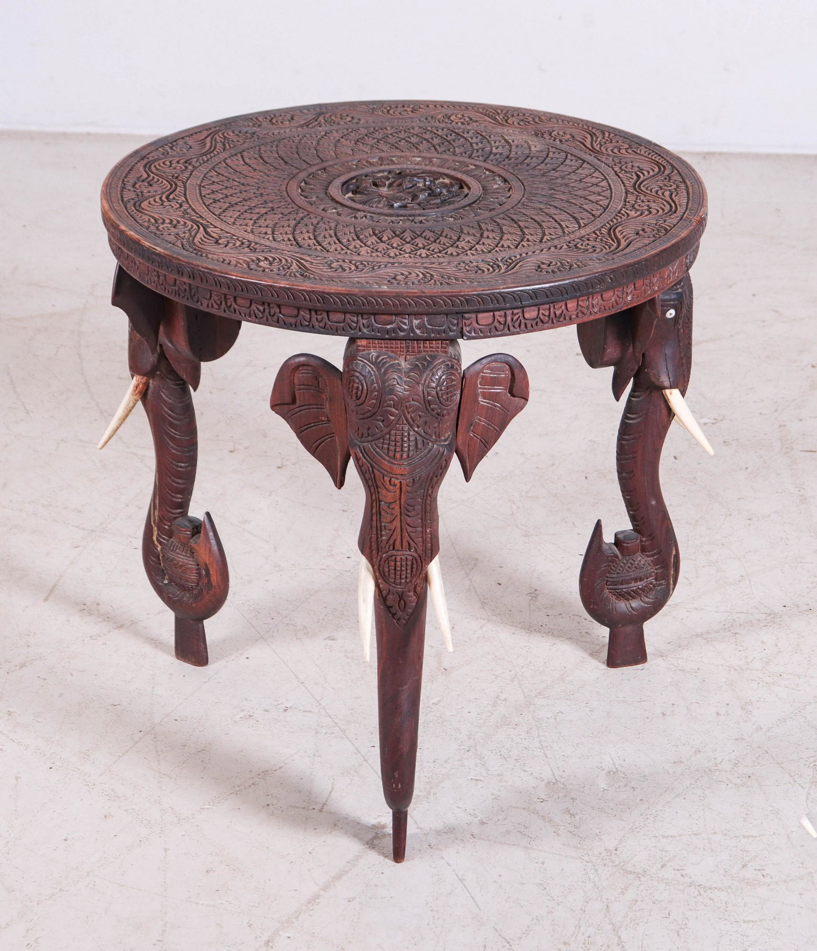 Indian carved side table w/ elephant heads: Indian carved side table w/ elephant heads, carved top with deity at center, elephant head legs with faux tusks, 21"h x 21"diameter