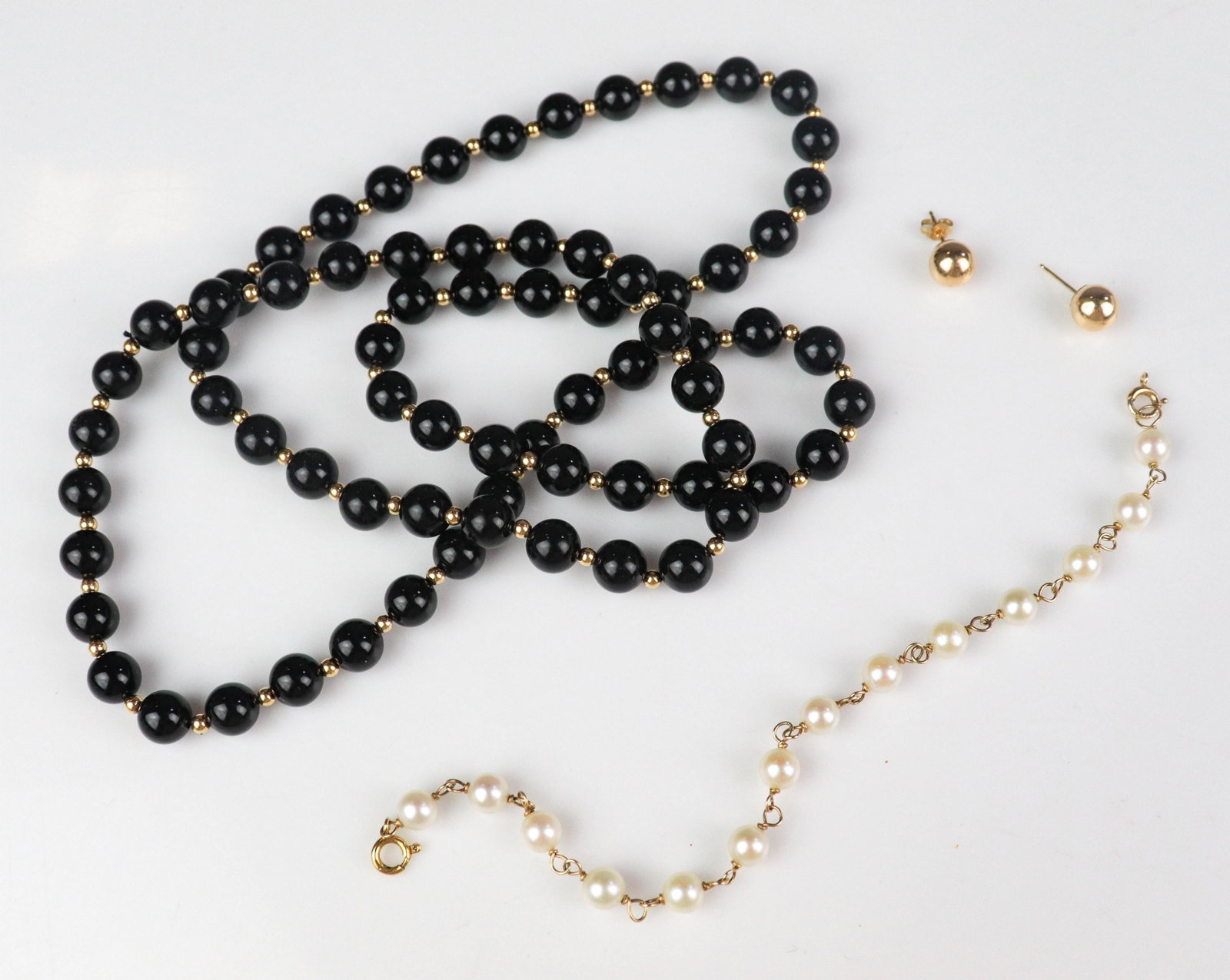14K Beaded Jewelry: 14K Yellow gold 6.0mm pearl bracelet; (1) pair of 14K Ball stud earrings, one missing butterfly friction backing, (1) onyx and gold bead necklace, 4.4 Dwt. (not including the onyx necklace)