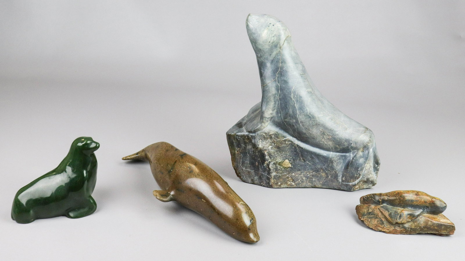 (4) Carved Stone Animals: (4) Carved stone animals, c/o gray seal signed "EJ" (11" h x 10" w), green seal signed "1190 RM" (4-1/2" h x 5" w), brown dolphin (13" l, missing stand, broken tail), brown seal Native Handcraft from 