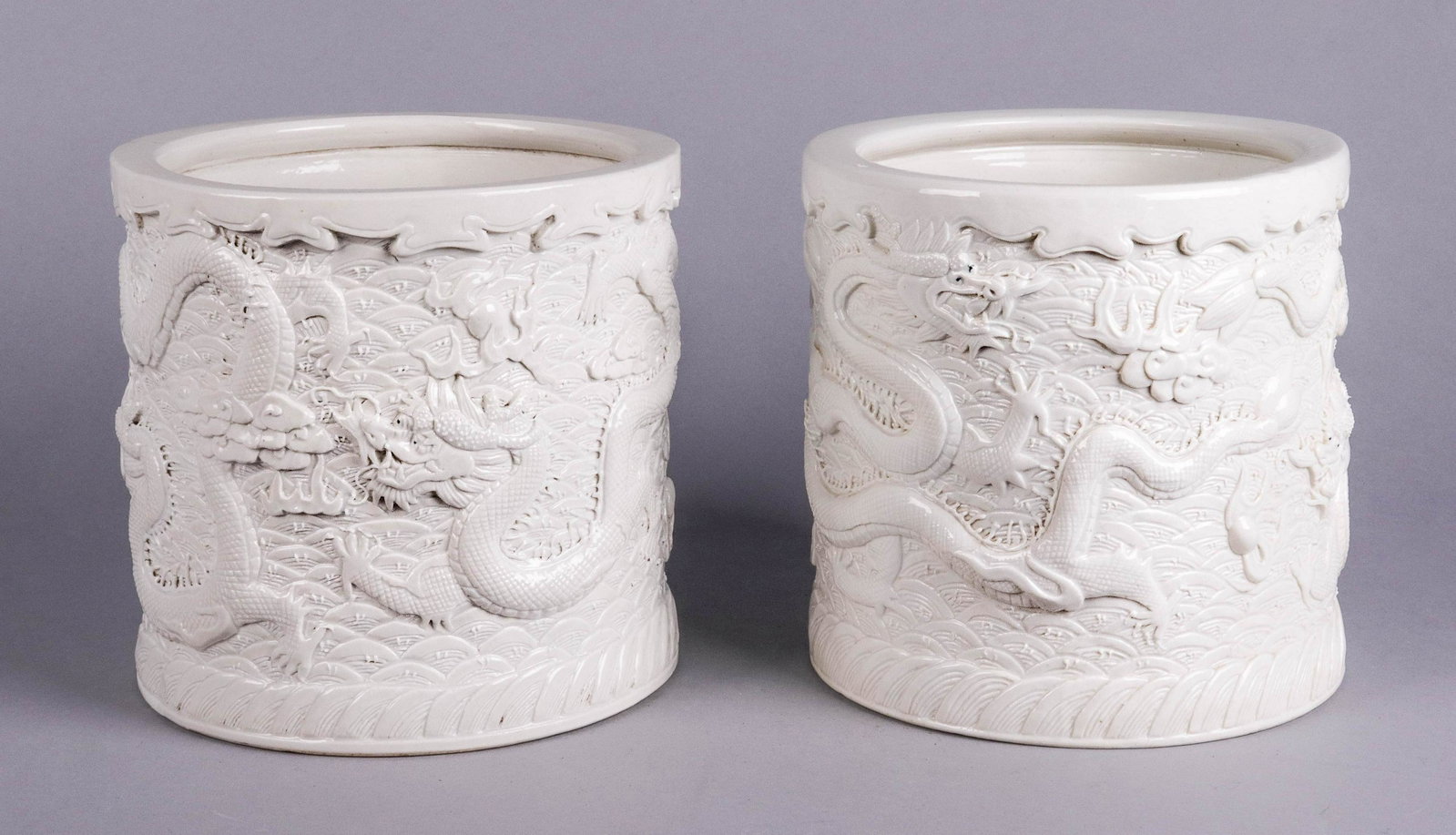 Pair of Wang Bingrong Dragon Brush Pots: Pair of Chinese carved porcelain brush pots, cream glazed, intricate dragon & flaming pearl design, cylindrical body, bearing mark of Wang Bingrong, 6-3/4" h x 7" dia & 6-3/4" x 7-1/2" dia, very good 