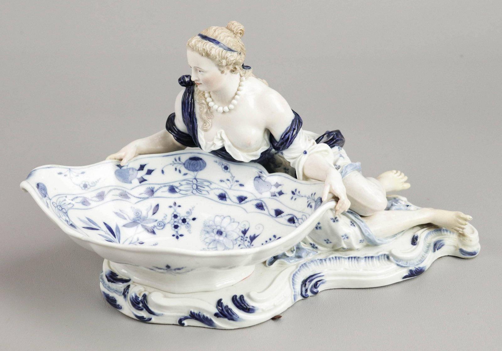 19th c. Meissen Figural Sweetmeat Dish: 19th c. Meissen figural sweetmeat dish, partially nude maiden in blue decorated garb, displaying blue onion serving dish raised on scroll decorated foot, 13"Lx7"H, potential repair at feet and (1) han