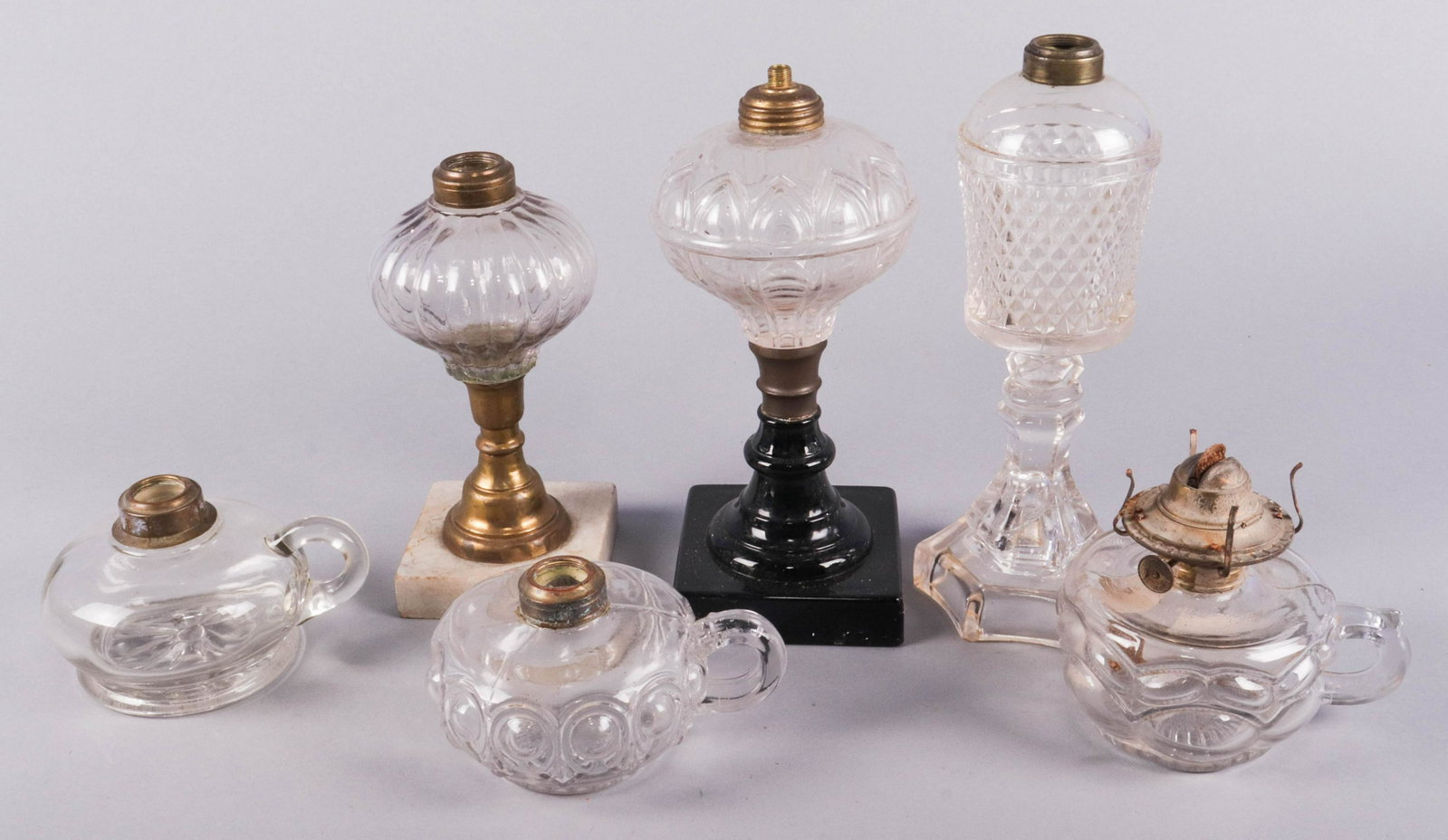 (6) Glass Oil Lamps: (6) Glass oil lamps to include flint glass whale oil lamp, 10-1/2"h, pressed glass lamp raised on black glass foot, 9-1/2"h, blown glass lamp on brass and marble foot, 8-1/2"h and (3) handled oil lamp