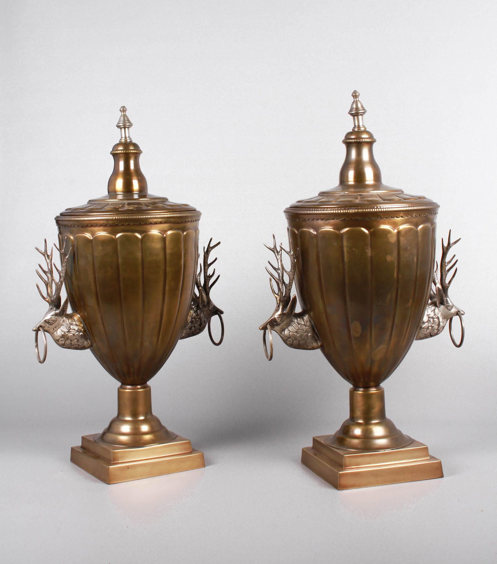 Pair Covered Trophy Urns: Pair covered trophy urns, gadrooned body and cover, ringed stag form handles at either side, tiered pedestal foot, 22" H, modern