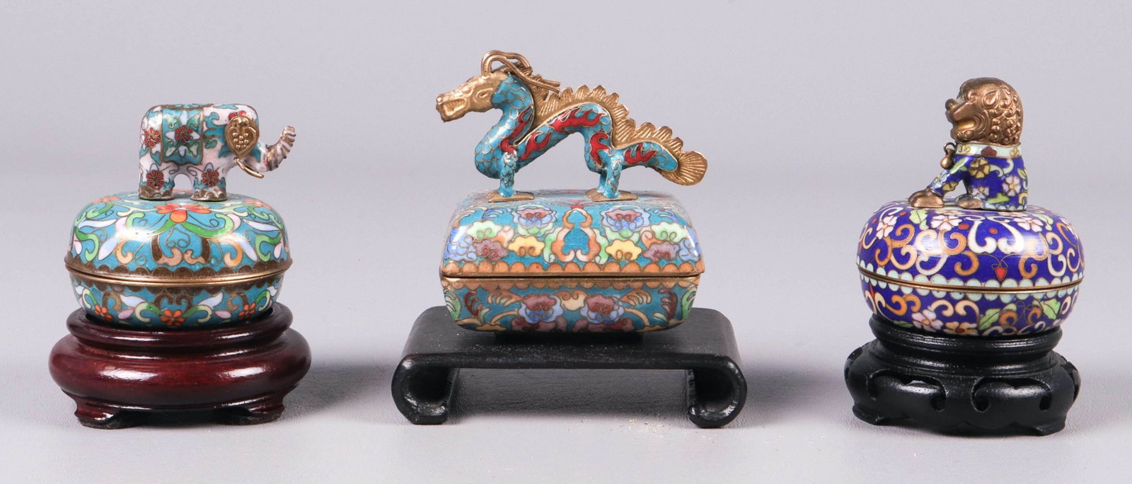 (3) Ardleigh-Elliott Cloisonne Music Boxes: (3) Ardleigh-Elliott cloisonne music boxes, 1992, c/o elephant No 73361, foo lion No 73362, dragon No 73362, on carved wood stands, largest 3" x 2-1/4" x 3-1/4" h, all in working condition