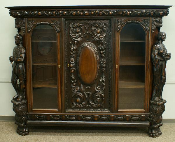 Massive carved walnut and walnut finished bookcase: Massive carved walnut and walnut finished bookcase with fully carved 3-dimensional figures at either side, a standing knight and a young maiden bearing a bowl of fruit, a fruit and leaf carved cornice