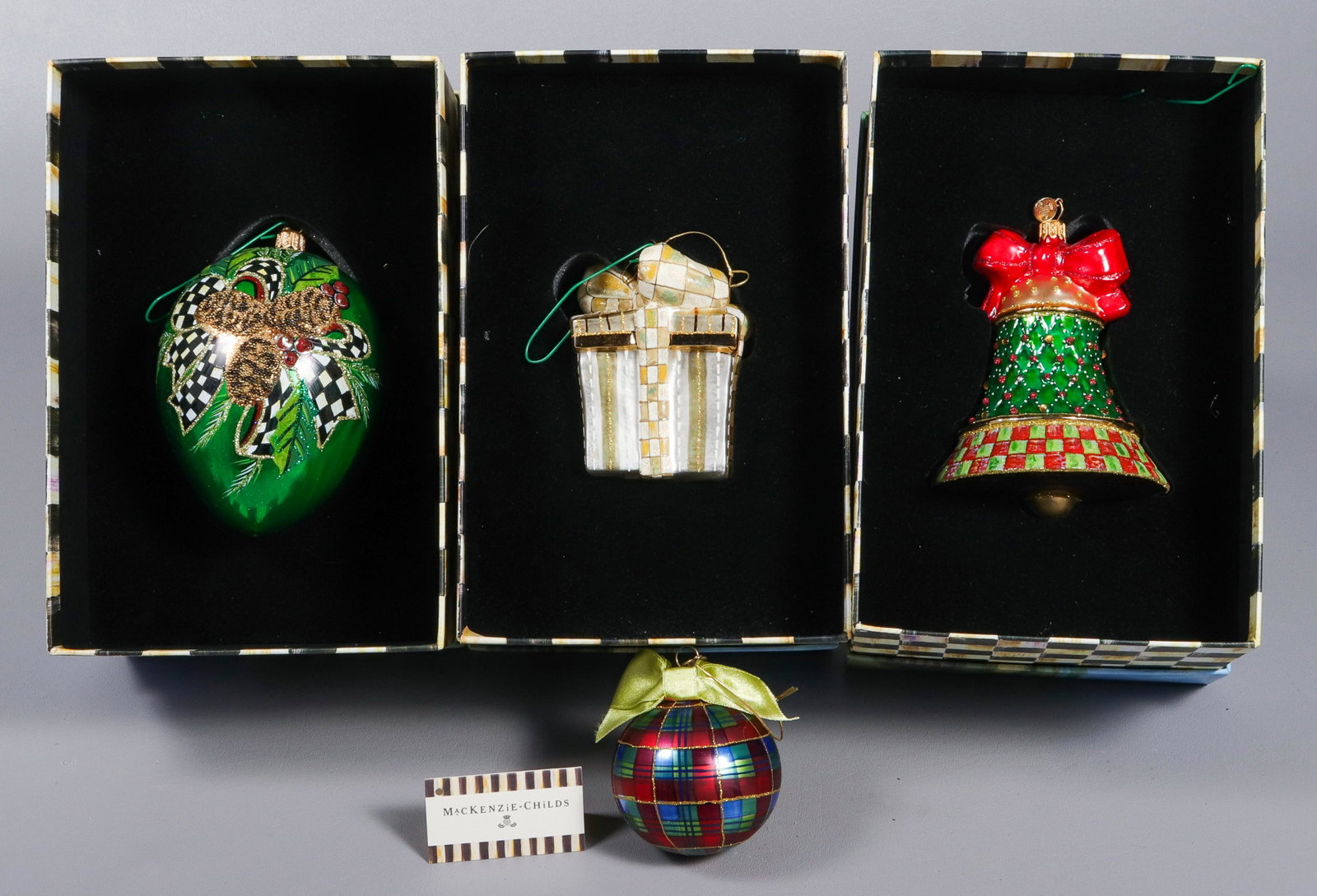(4) Mackenzie Childs Christmas Ornaments: (4) Mackenzie Childs glass Christmas ornaments, (3) with original boxes, c/o tartan ball, Orchard Check Bell, Parchment Check Present, Evergreen Pinecone