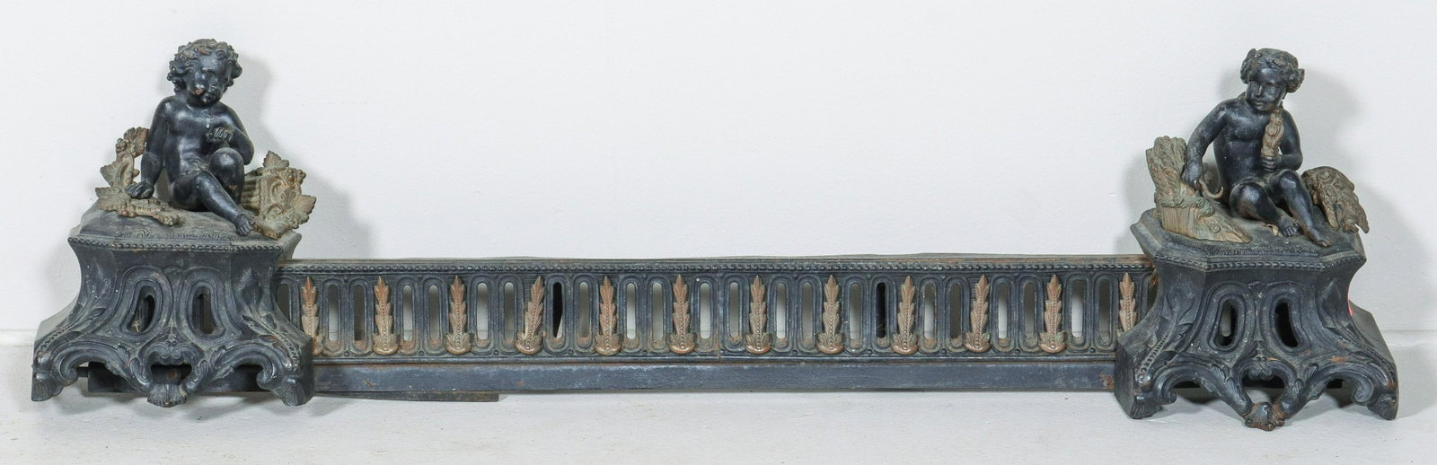 French Black Iron Putti Mounted Fire Fender: French black iron putti mounted fire fender, pierced fender with leaf joined decoration, putti figures at either end, from which fender is expandable, 38" to 43" maximum.