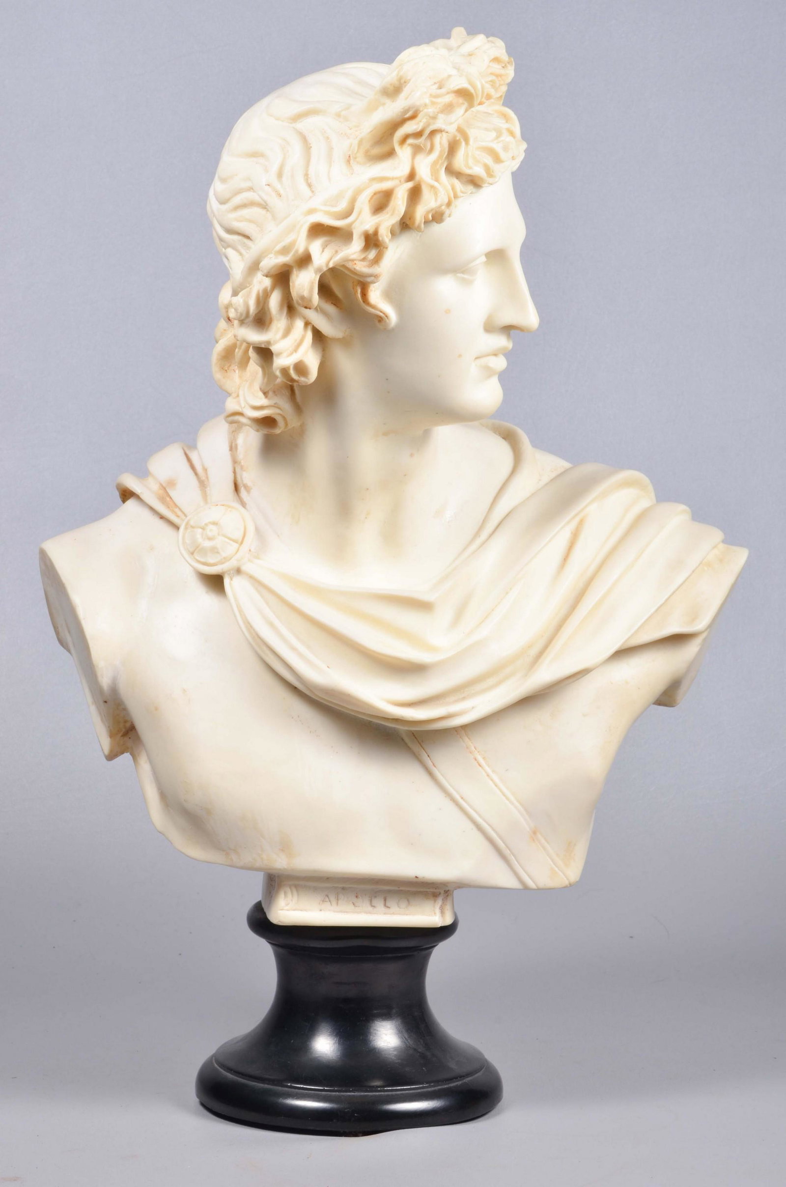 Italian Carved Composite Bust of Apollo: Italian carved composite bust of Apollo, marked made in Italy at underside, on joined black pedestal base, 22-1/4" H