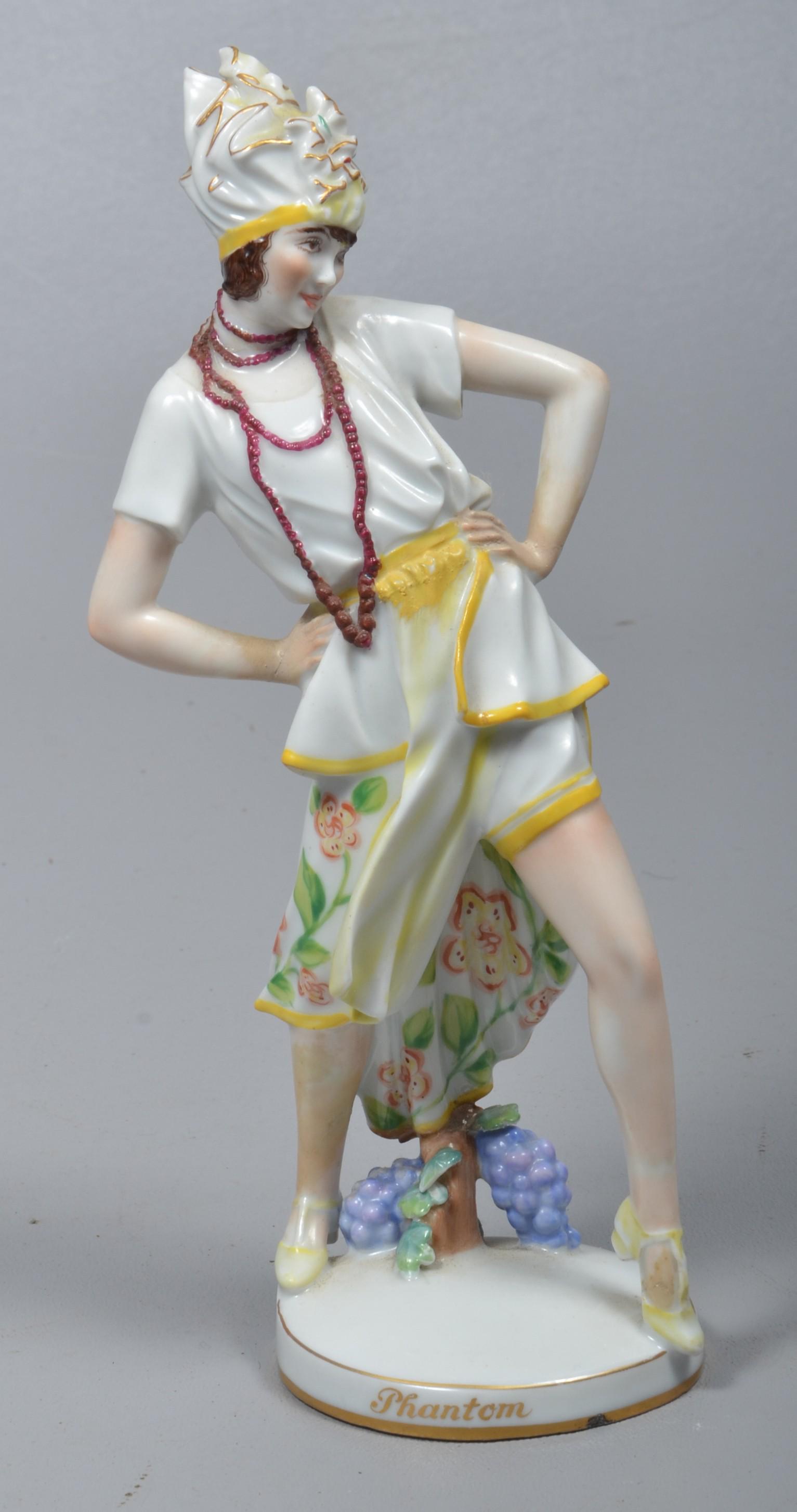 Augarten Wien Vienna Porcelain Flapper Figure: Augarten Wien Vienna porcelain flapper figure, grape bunches and vine at feet, her leg outstretched with hands on hips, multi-strand necklace and parcel gilt hat, 'Phantom' at bottom, repair to back l